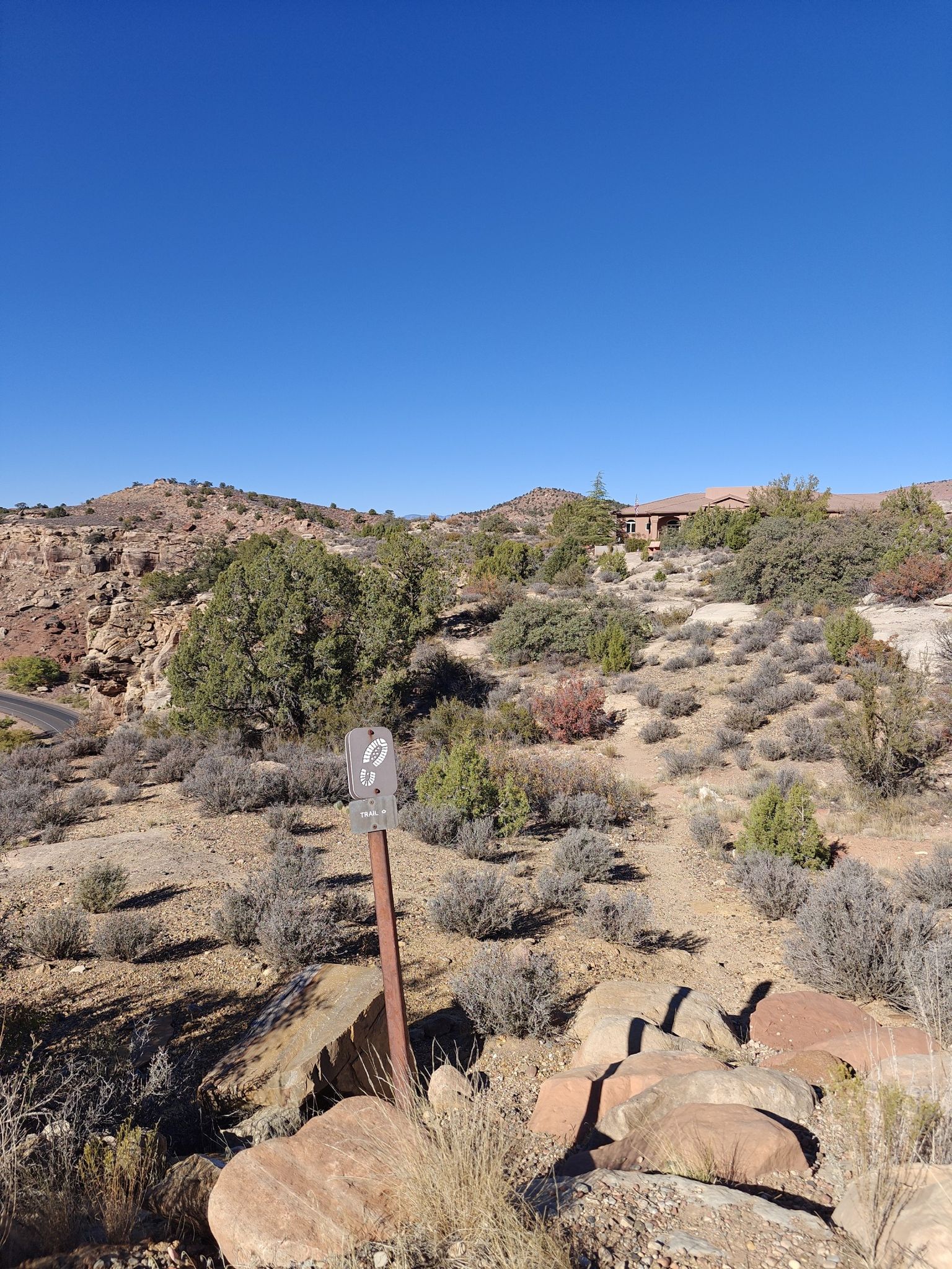 Small sign on a post in a sunny, arid, rocky landscape with distant hills. - Chinle Trail