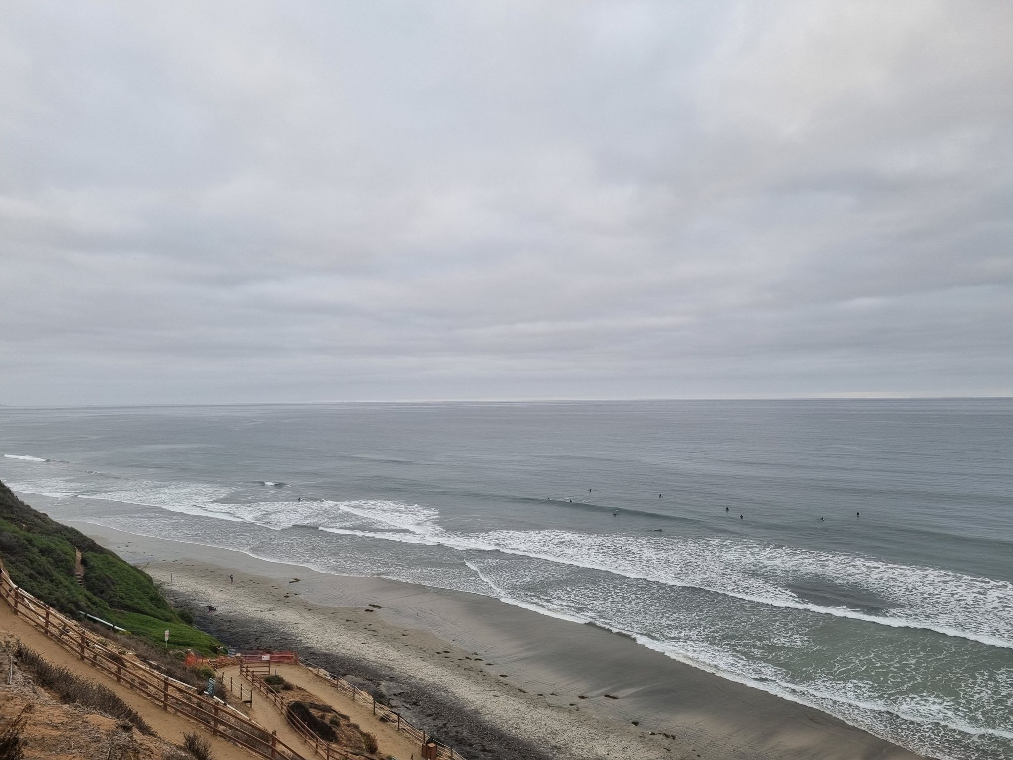 Overcast ocean view with waves, sandy beach, and people in water. - San Elijo Lagoon Estuary Canal – Swami's Seaside Park loop from Cardiff State Beach
