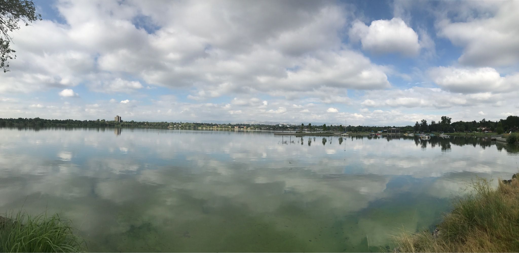 Panoramic view of a lake reflecting a cloudy sky, with distant shore. - Hiking loop from Edgewater