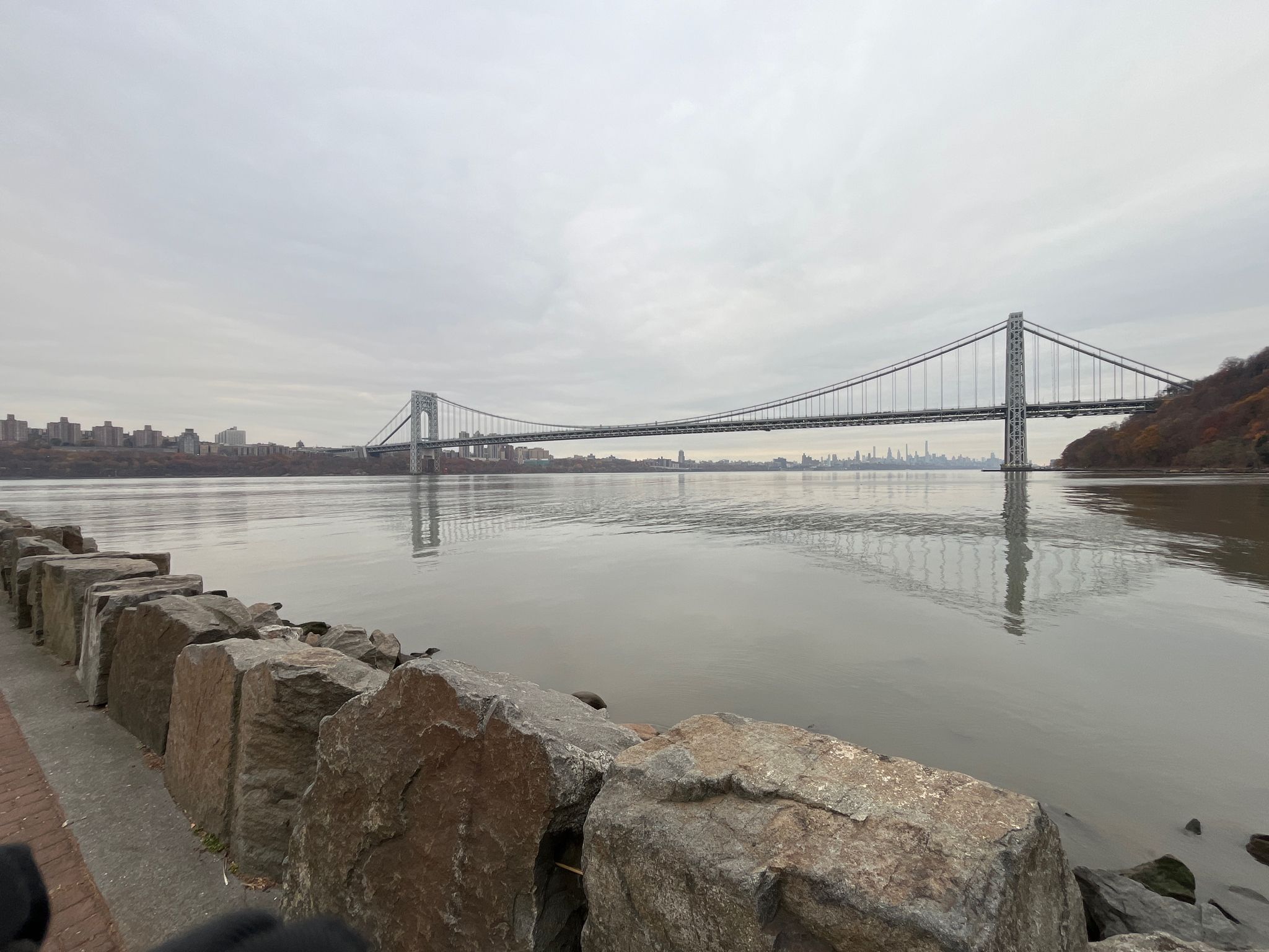 Suspension bridge over a wide river with a city skyline under cloudy sky. - Ross Dock Picnic Area – Edgewater Entrance loop from Fort Lee