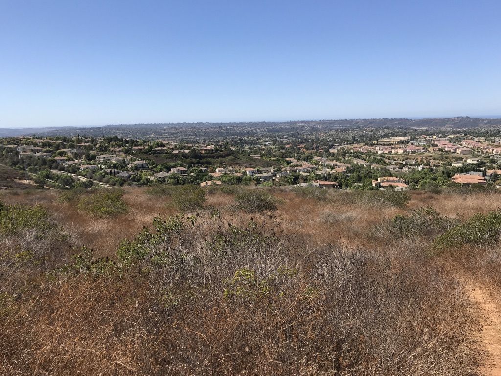 Expansive view of a town in a valley with dry brush foreground, bright sky. - Denk Mountain loop from La Costa Canyon High School