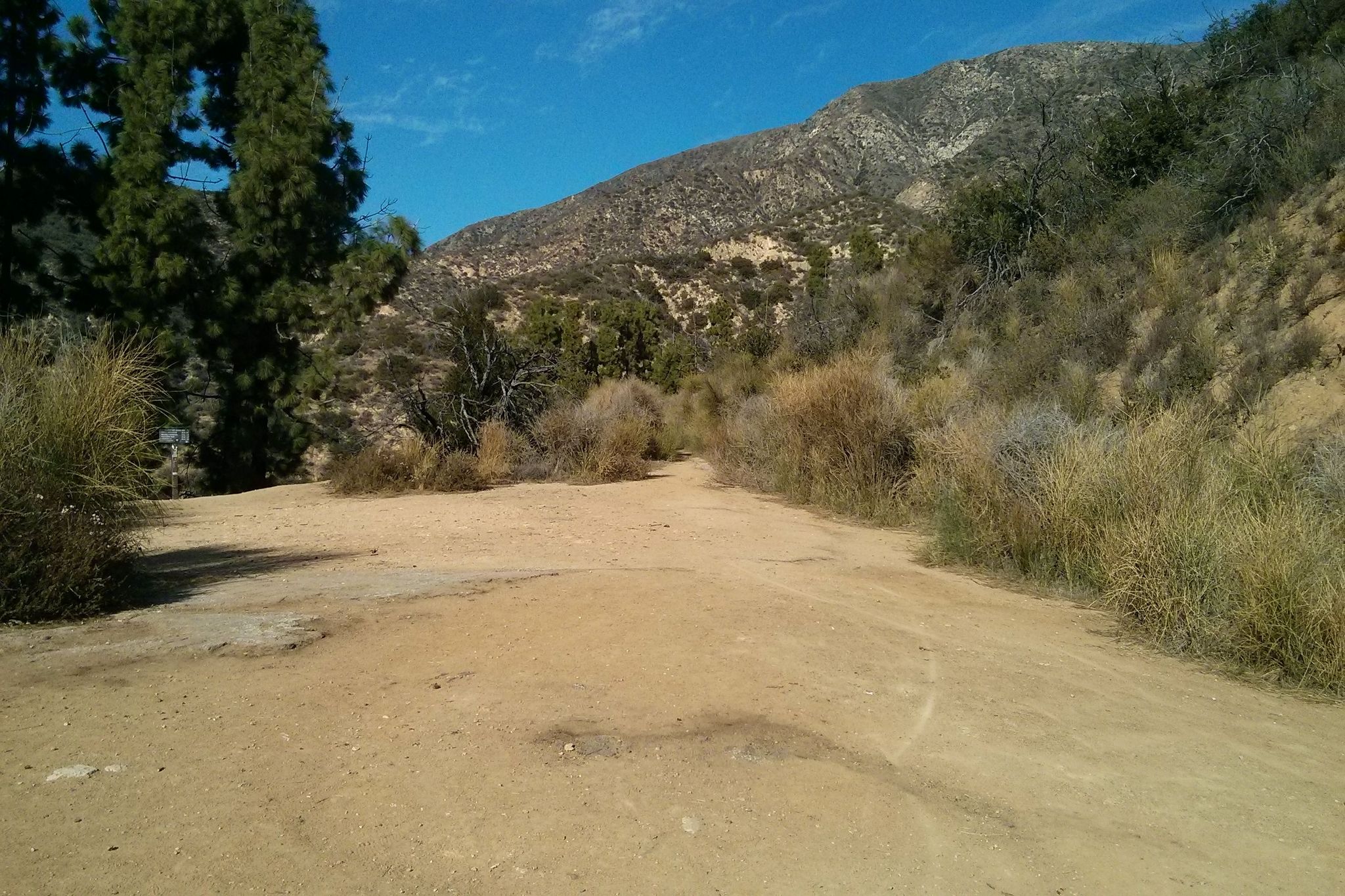 A wide dirt path leads towards a large mountain under a clear blue sky. - Wella's Peak – El Prieto Trail loop from Altadena