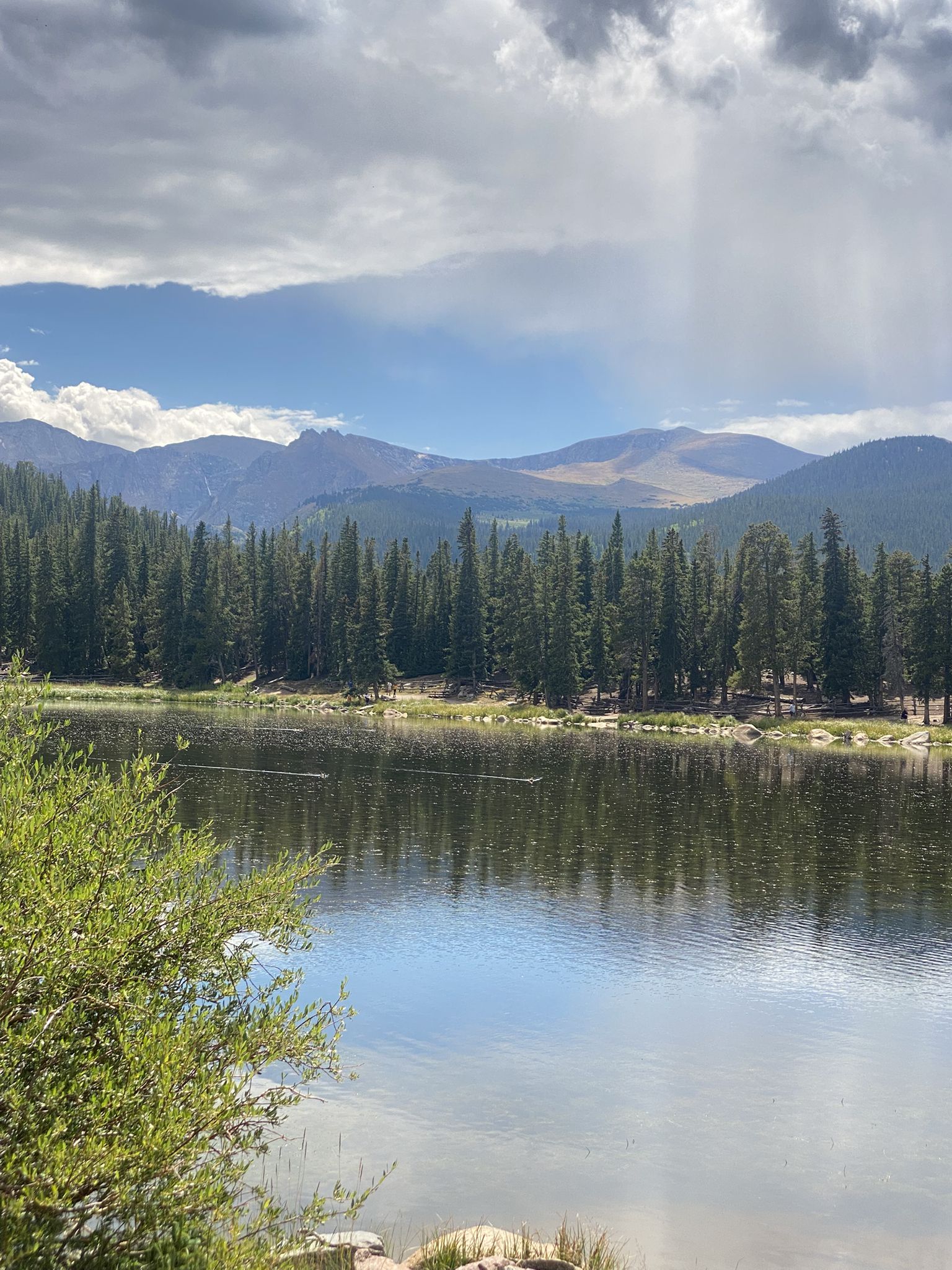 Lake with pine trees, distant mountains, and cloudy sky with light rain. - Idaho Springs to Mount Blue Sky (Evans) Summit