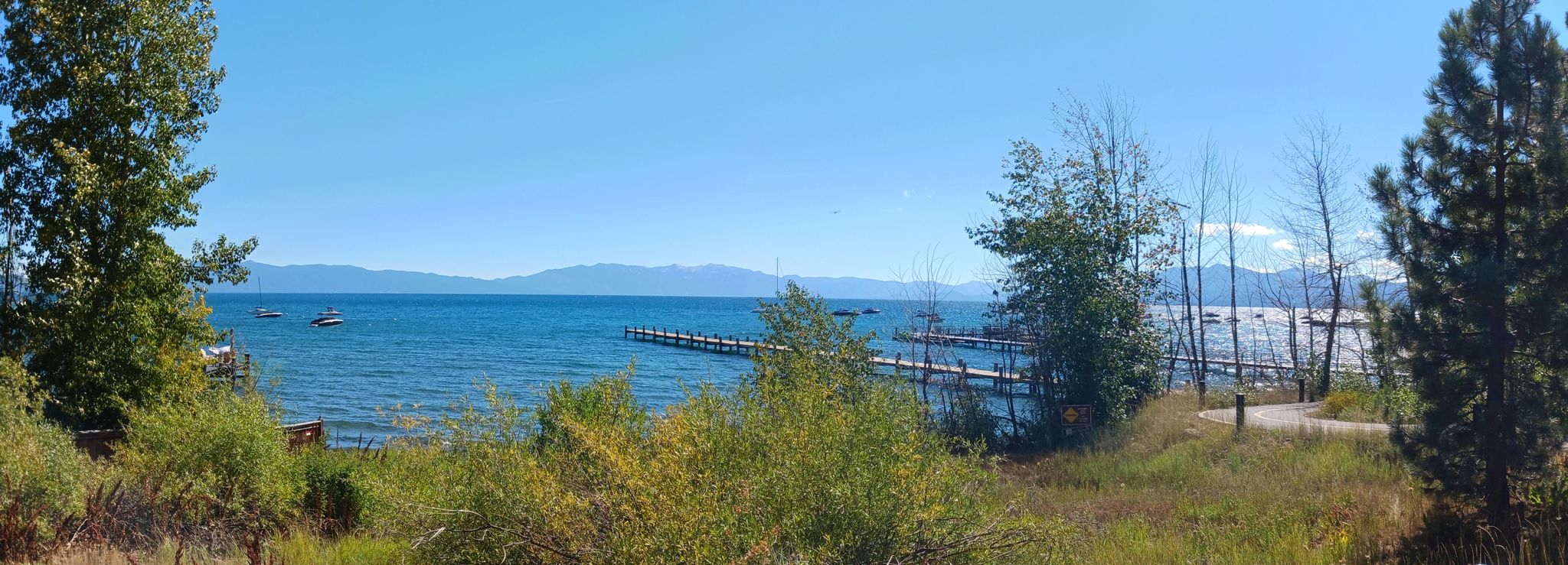 Panoramic view of a blue lake with piers, boats, and distant mountains. - Tahoe City Marina loop from Burton Creek State Park