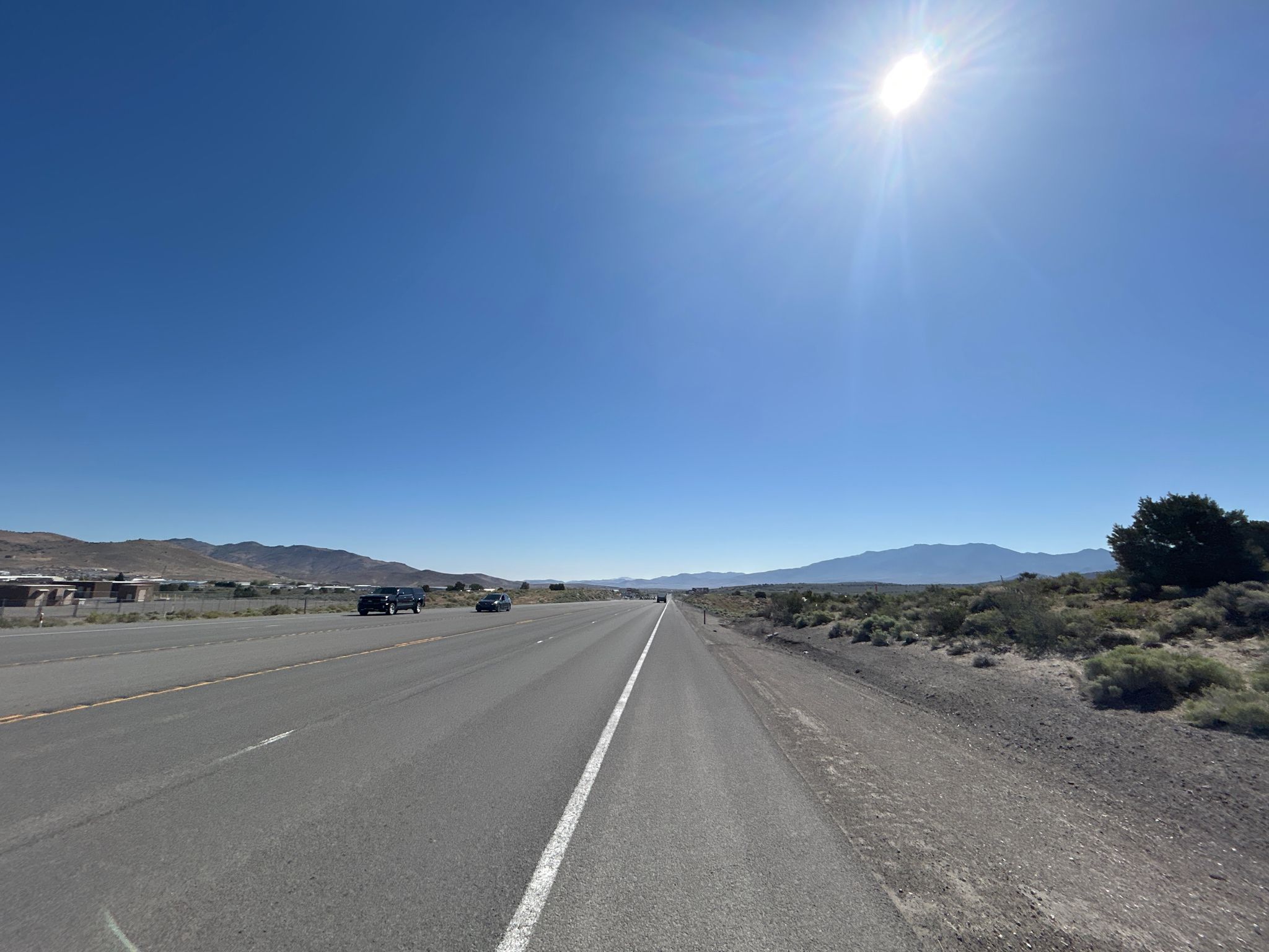 A long, straight highway stretches through an arid landscape under a bright sun. - South Reno to Carson City & Virginia City loop