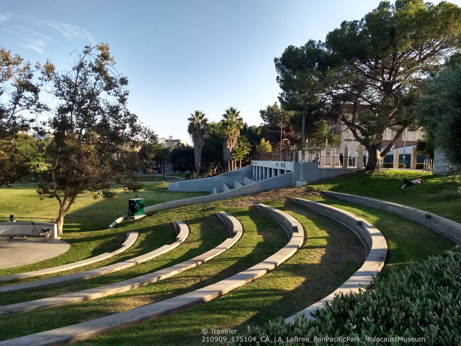 Curved concrete steps on a grassy slope in a sunny park with trees. - Pan Pacific Park Trail