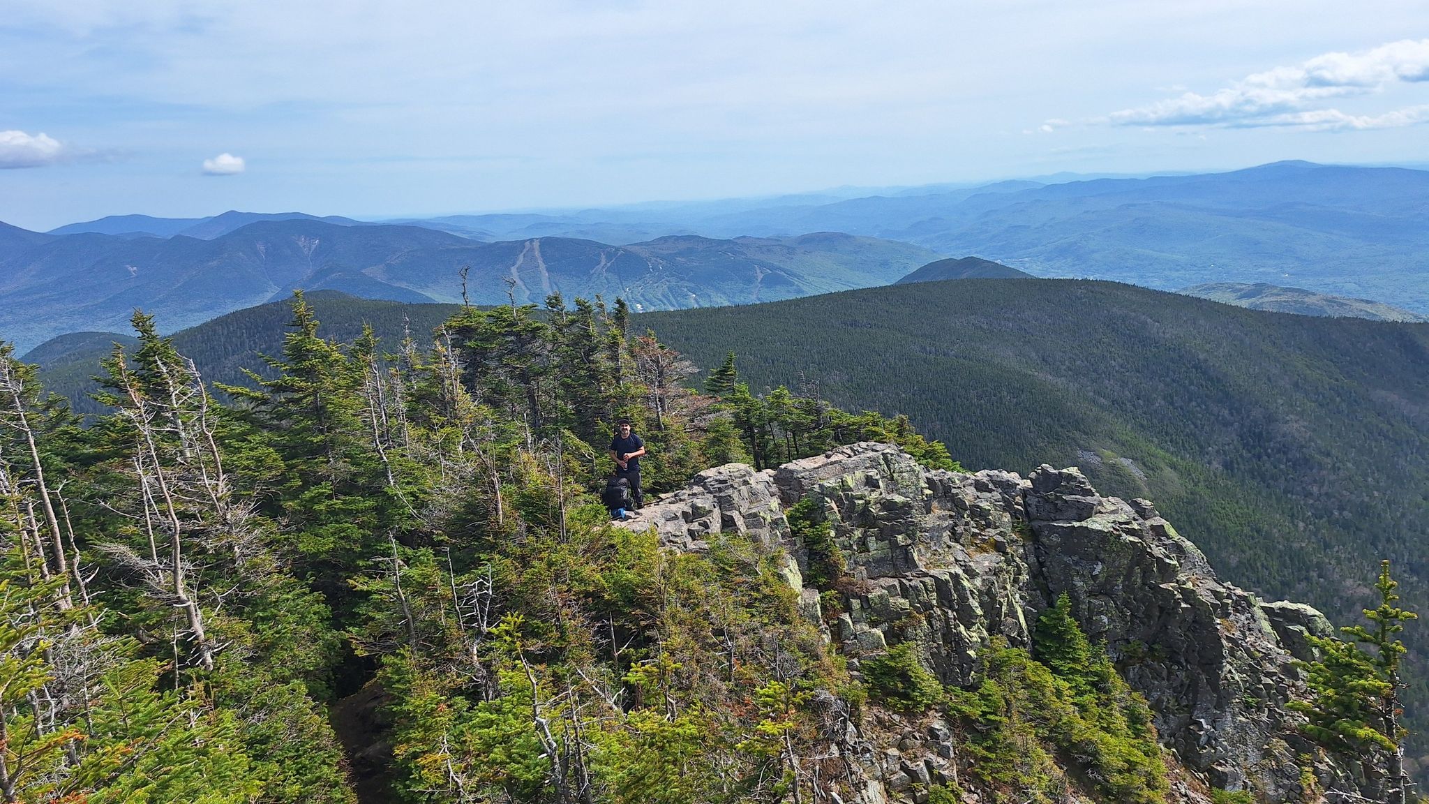 Person standing on a rocky mountain ridge with distant peaks under a sunny sky. - Old Osseo Trail to Mount Flume