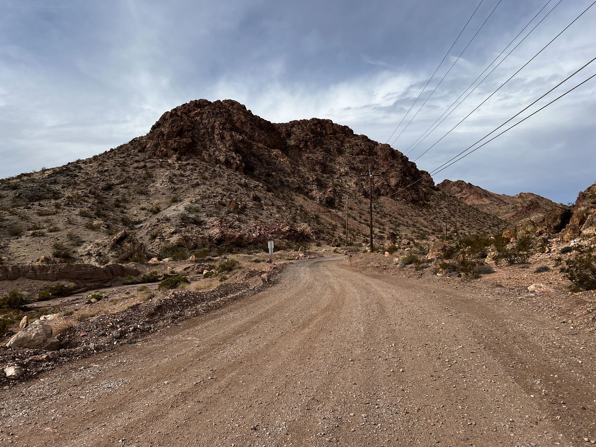 A wide dirt road winds through arid, rocky mountains under an overcast sky. - Par None, IMBA, and POW loop — Bootleg Canyon