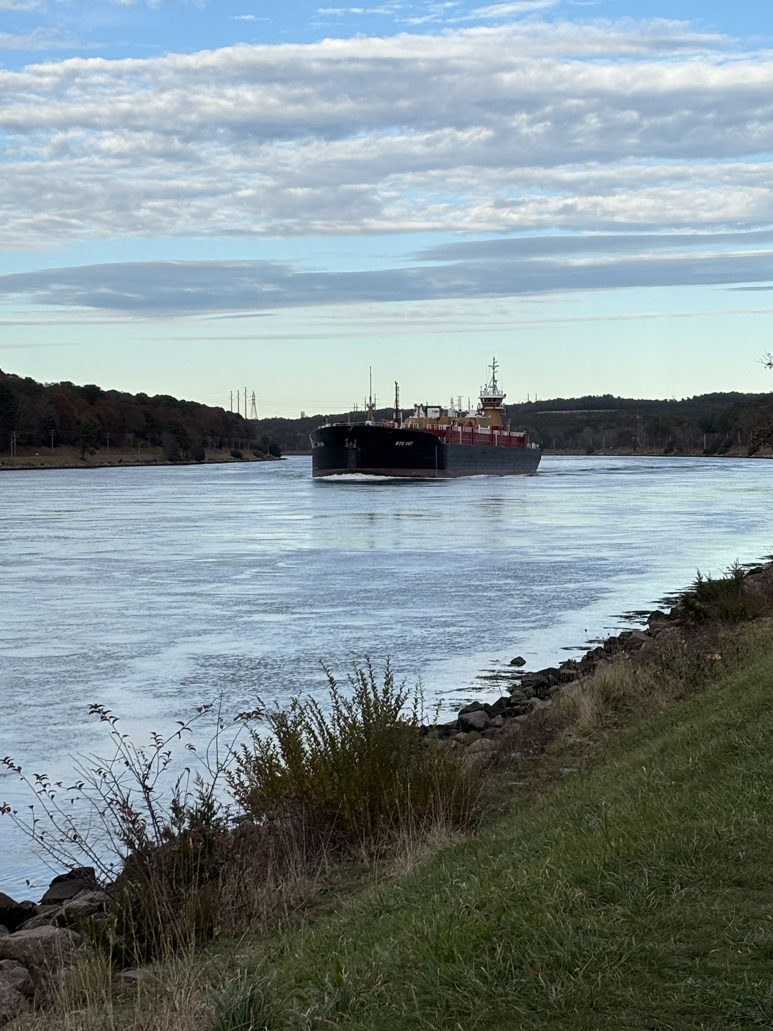 Large cargo ship sailing on a wide waterway under a partly cloudy sky. - Cape Cod Canal Bikeway – Sagamore Bridge loop from Buzzards Bay