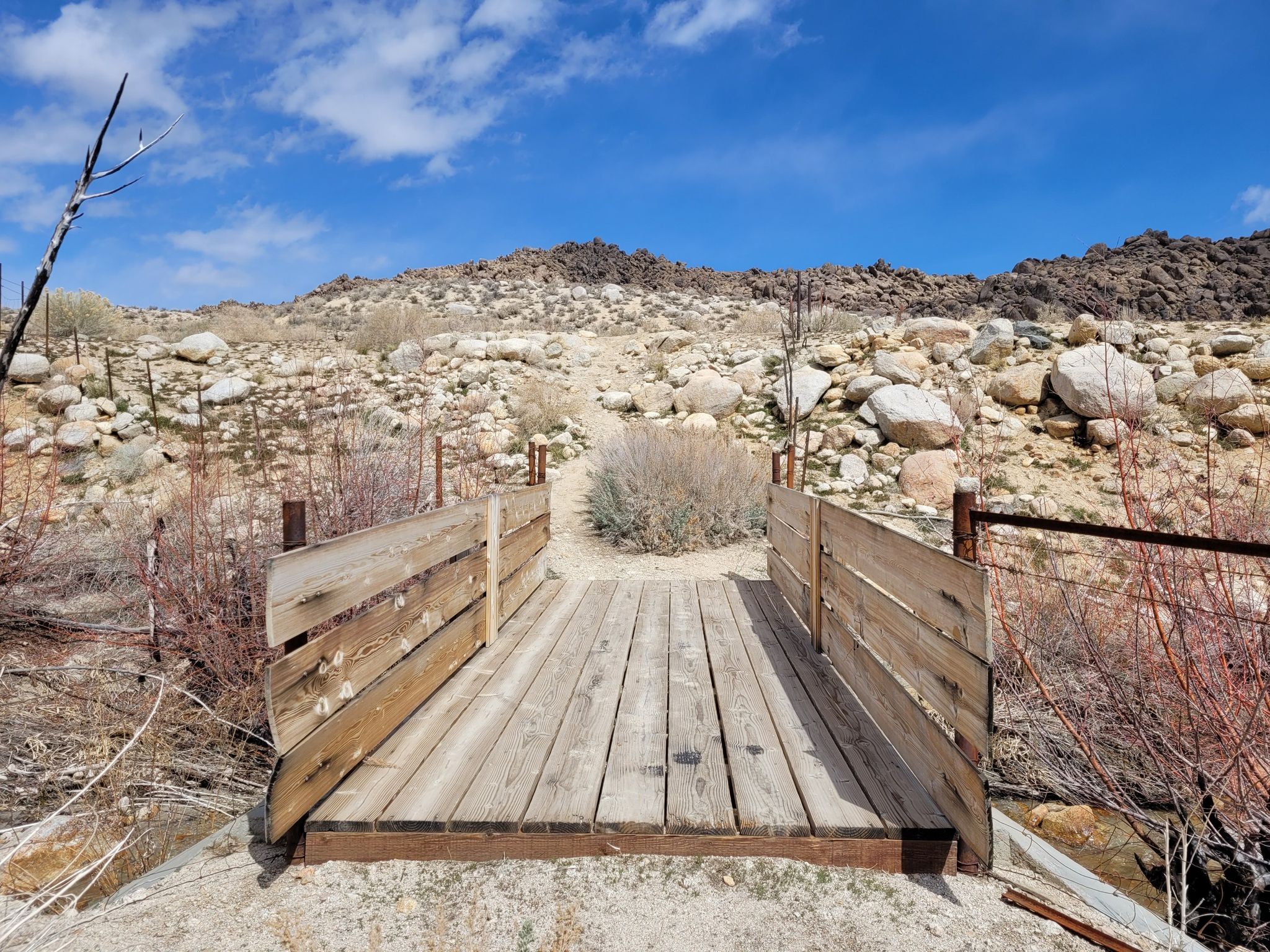 Small wooden footbridge over dry ground in a rocky, arid landscape. - Upper Alabama Hills Trail to Cyclops Skull Arch