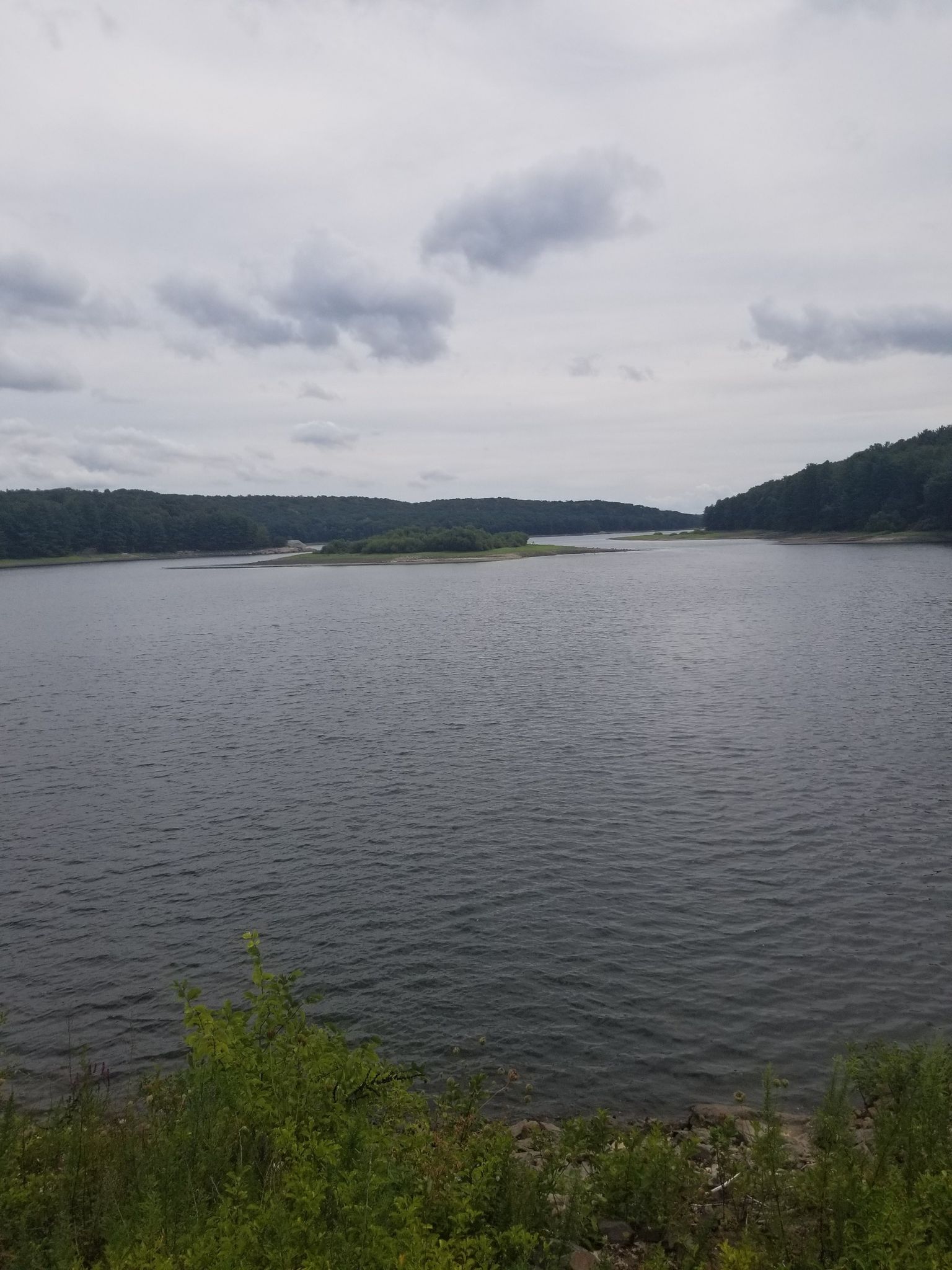 A vast lake stretches under a cloudy sky, surrounded by distant green hills. - View of Saugatuck Reservoir – View of Saugatuck Reservoir loop from Danbury