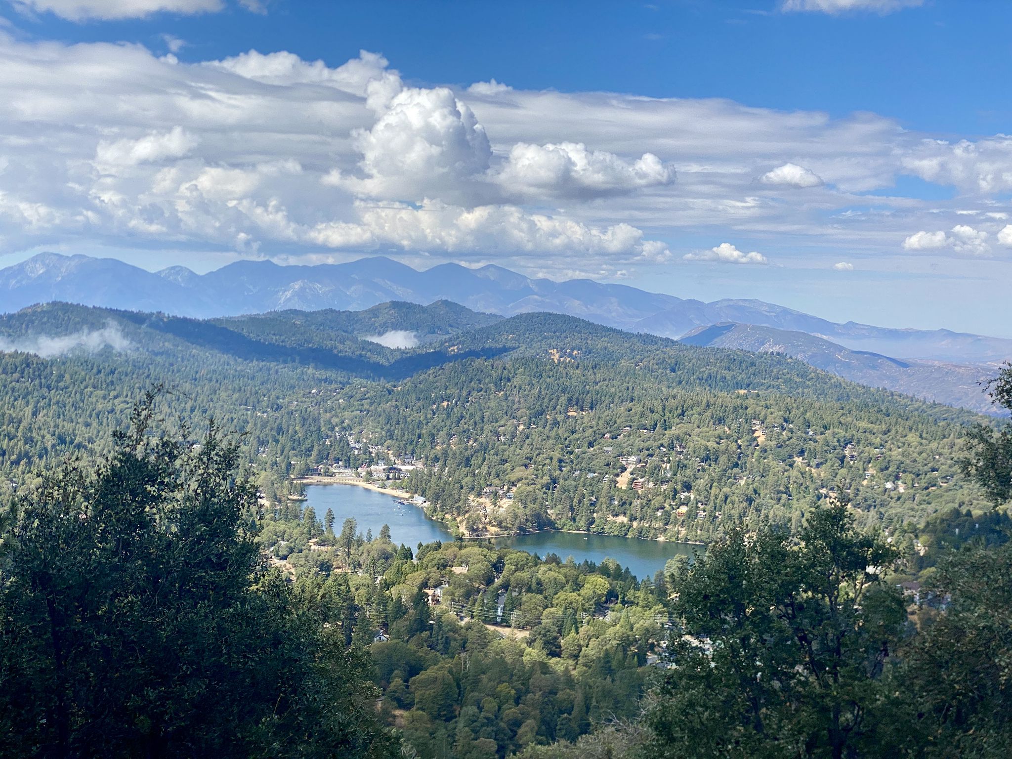 Aerial view of a blue lake nestled among green, forested mountains under a cloudy sky. - Lake Arrowhead, Lake Gregory, Running Springs, and Keller Peak loop