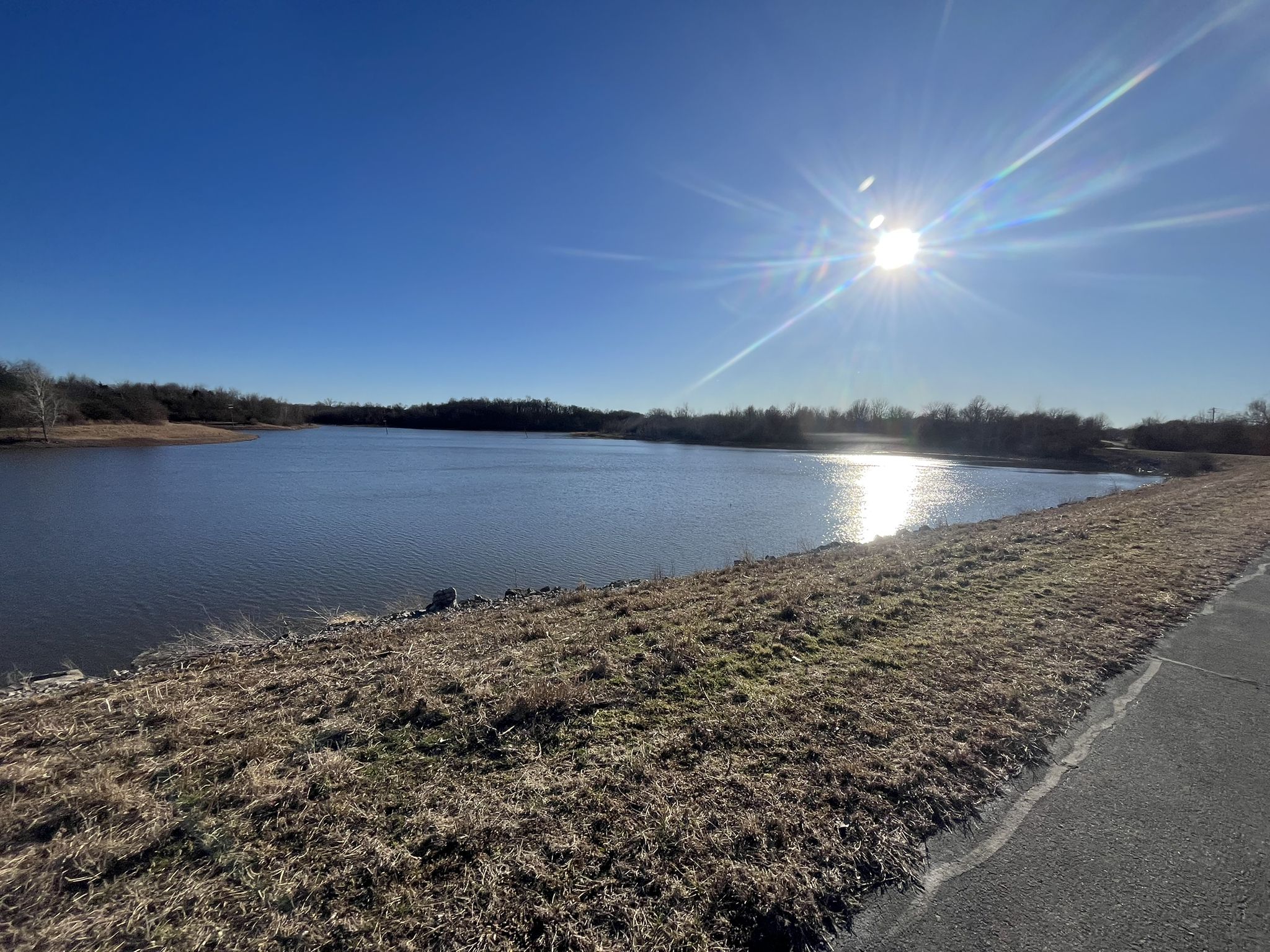 Sunny day over a wide lake with dry grass and a paved path. - Lake St. Louis – Mononame 207 Reservoir loop from Weldon Spring Heights