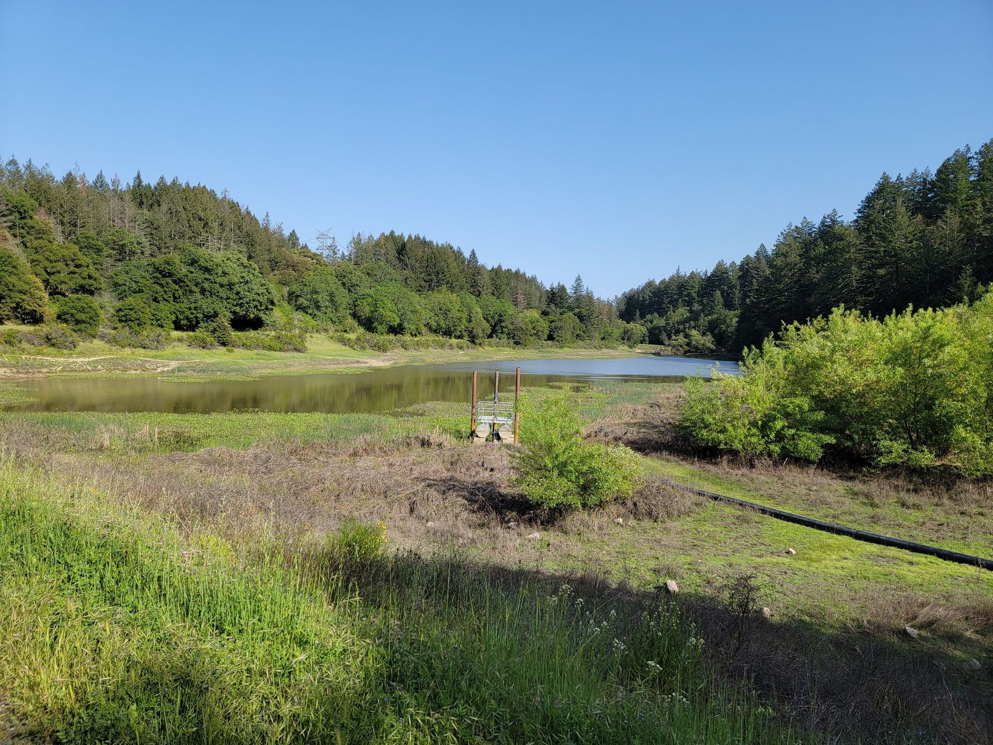 A lake with a small structure, surrounded by grassy banks and forested hills. - Summit of Sanborn County Park – John Nicholas Trail Viewpoint loop from Sanborn County Park