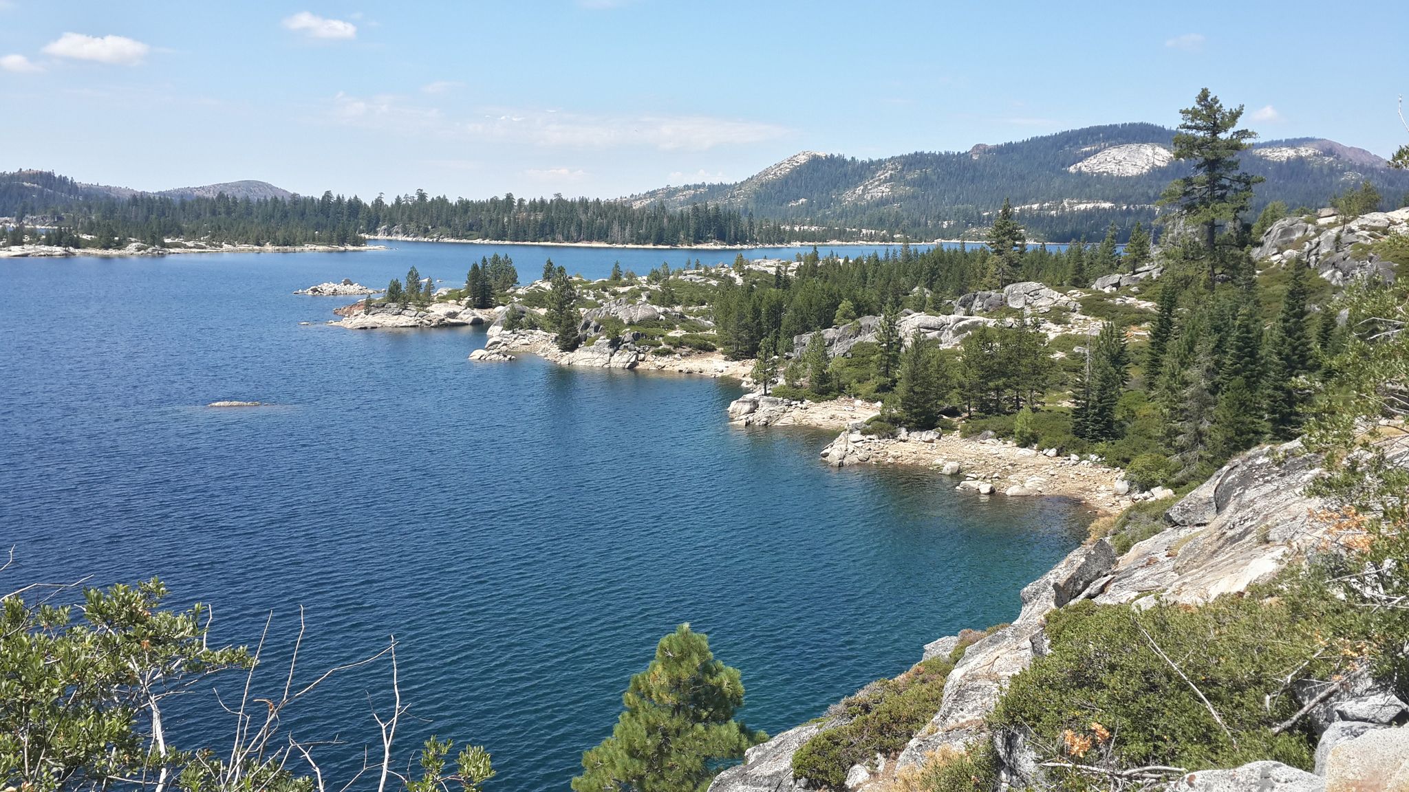 Sunny view of a blue lake with rocky shores and pine trees. - Loon Lake via Rubicon Trail