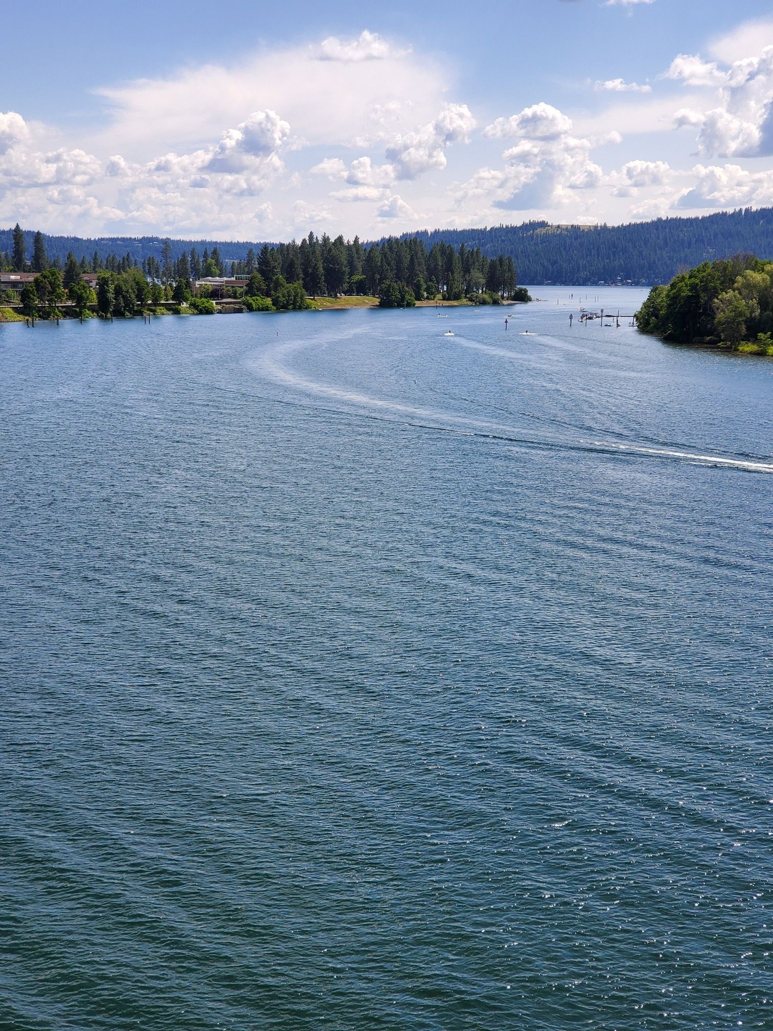 Wide blue lake with boat wakes, forested shores under a sunny sky. - North Idaho Centennial Trail
