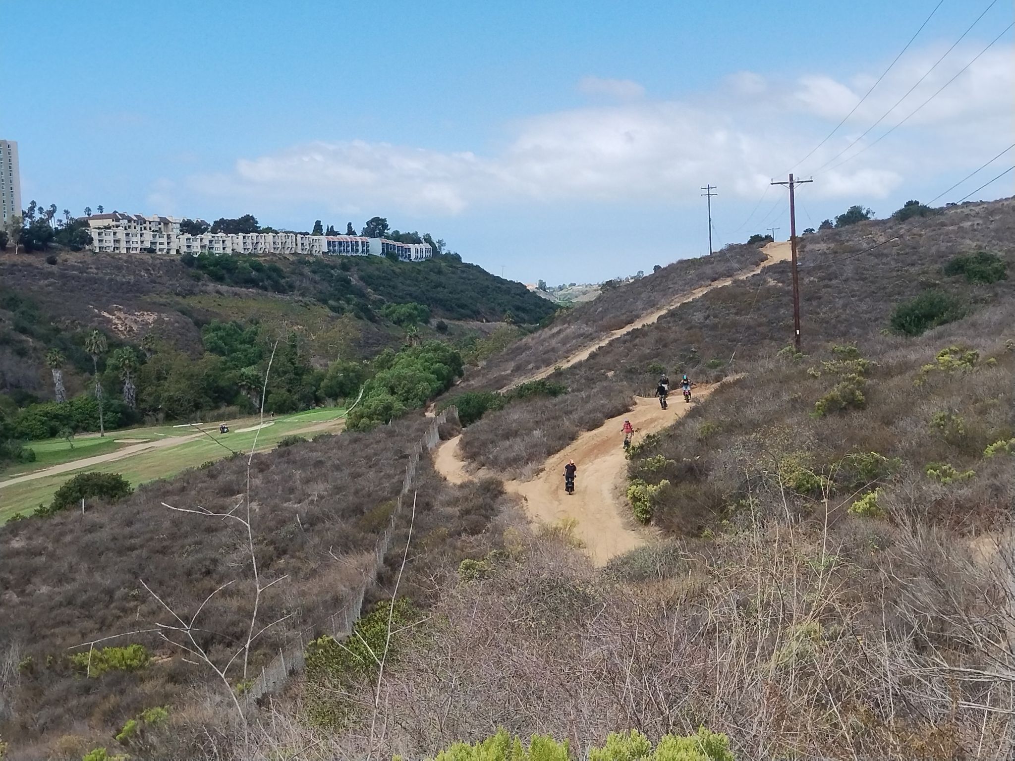 People hike a winding dirt path up a dry, brushy hillside. - Tecolote and Rose Canyon Loop