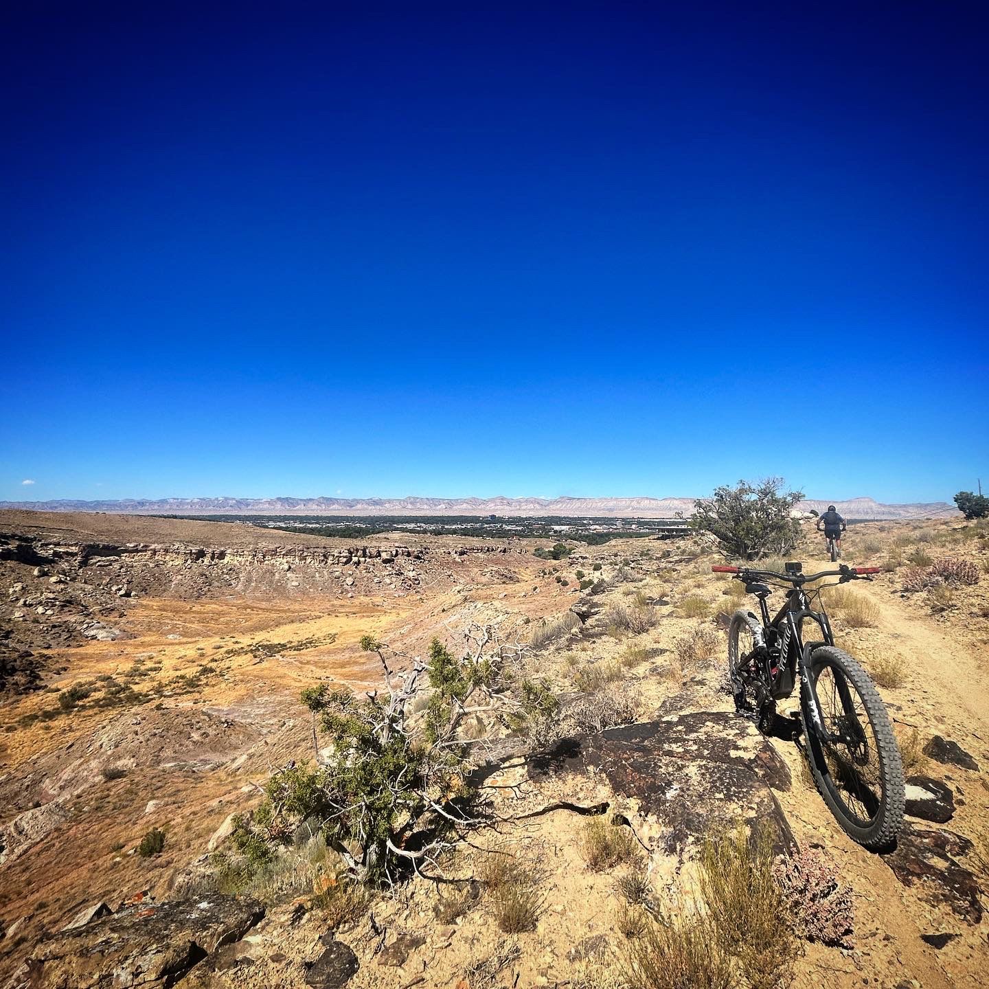 A mountain bike parked on a sunny, arid ridge overlooking a vast valley. - Monument Corridor Trail – Tabeguache Trailhead loop from Colorado River