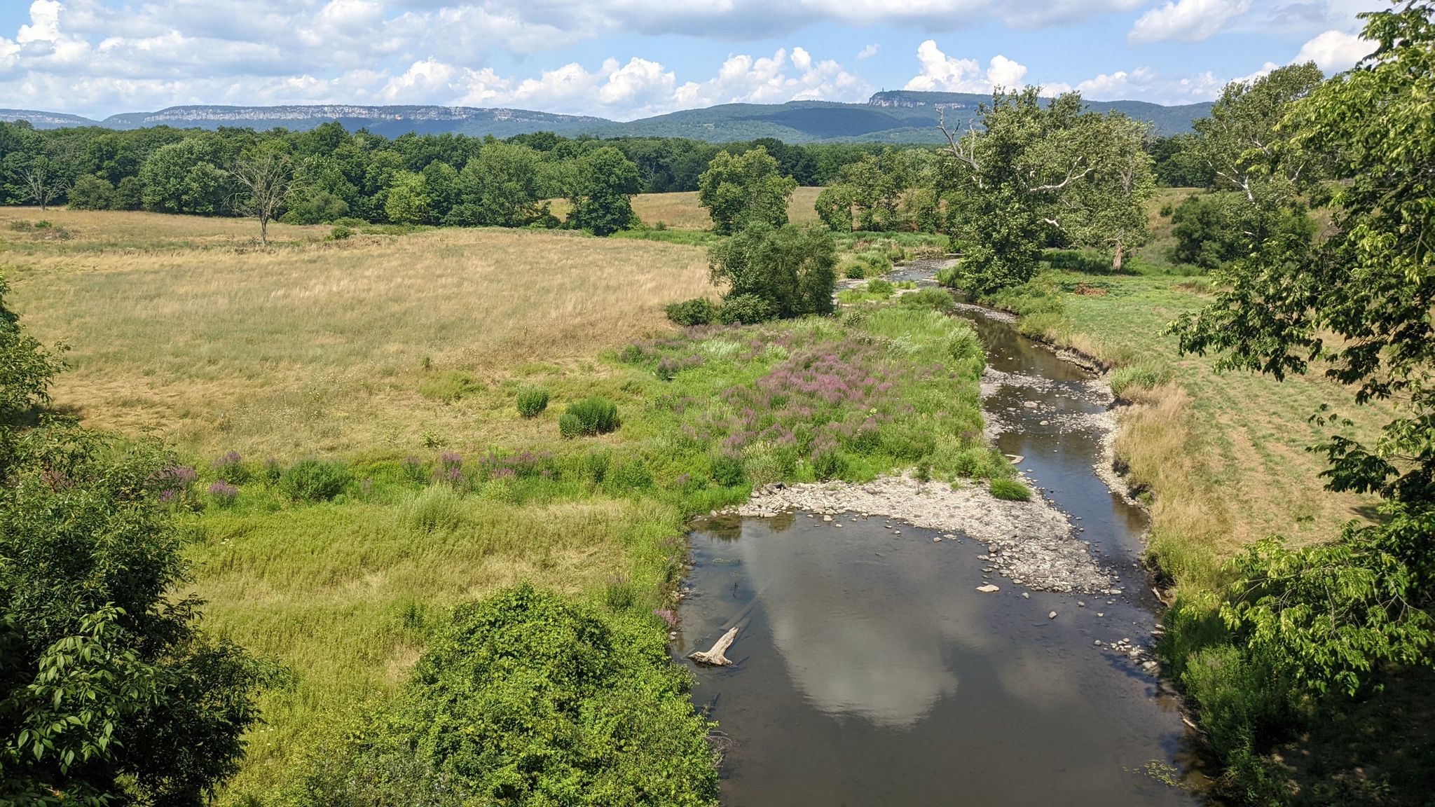 Aerial view of a winding river through green fields under a cloudy sky. - Wallkill Valley Rail Trail