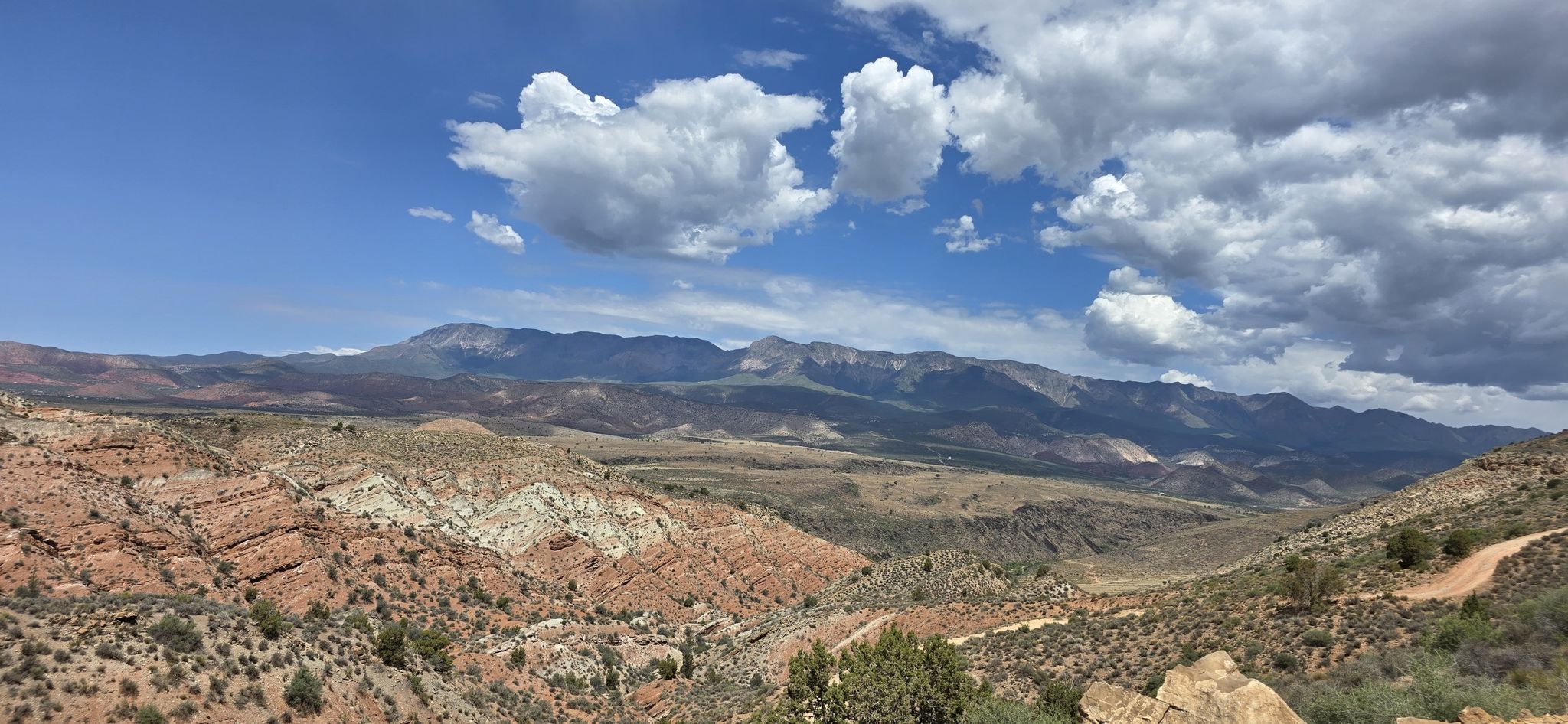 Vast desert landscape with rocky hills, distant mountains, and a dirt road under a cloudy sky. - Toquerville Falls