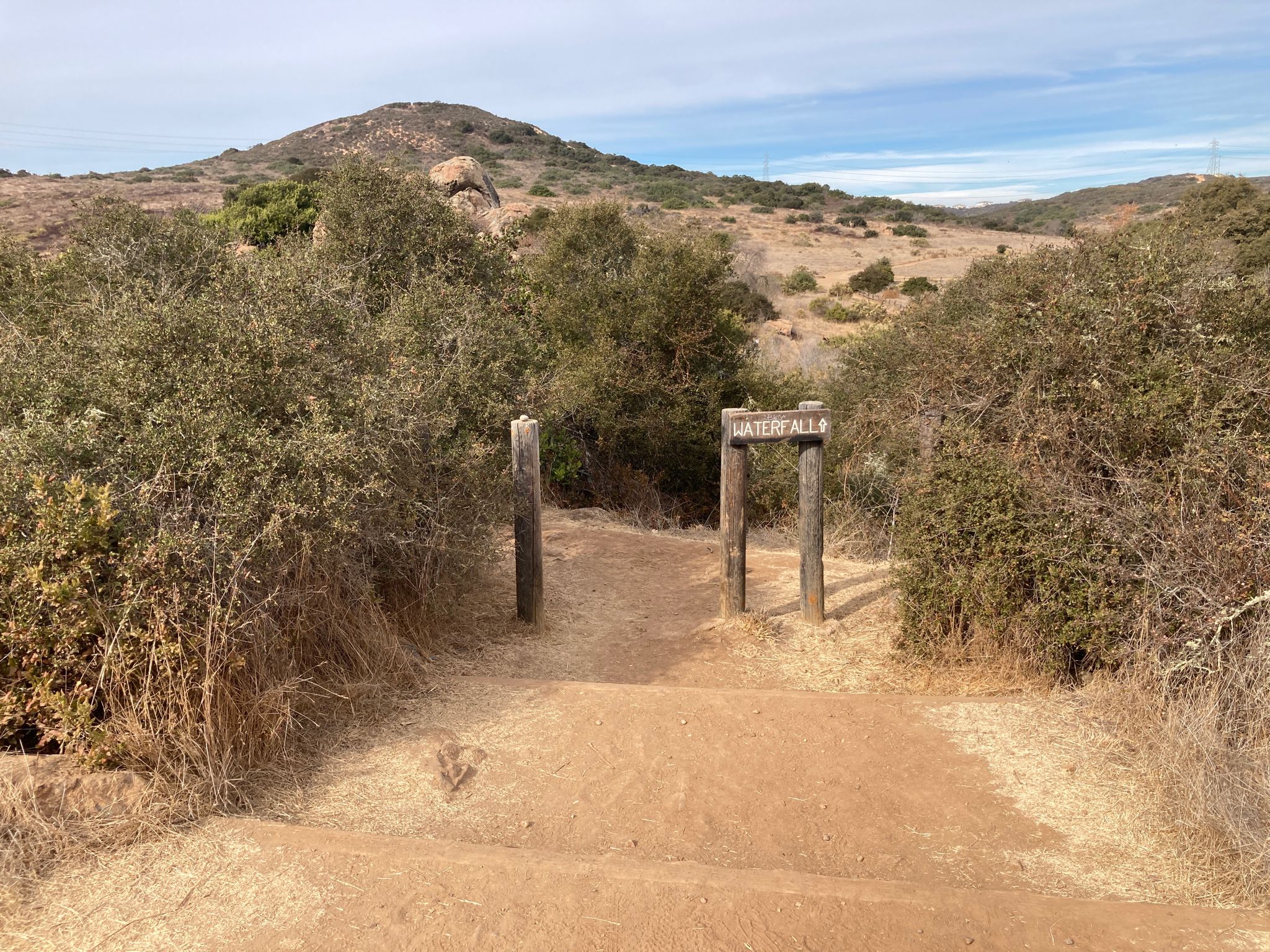Dirt path leading to a wooden signpost among dry, brushy hills. Bright daylight. - Los Peñasquitos Falls loop from Lopez Canyon