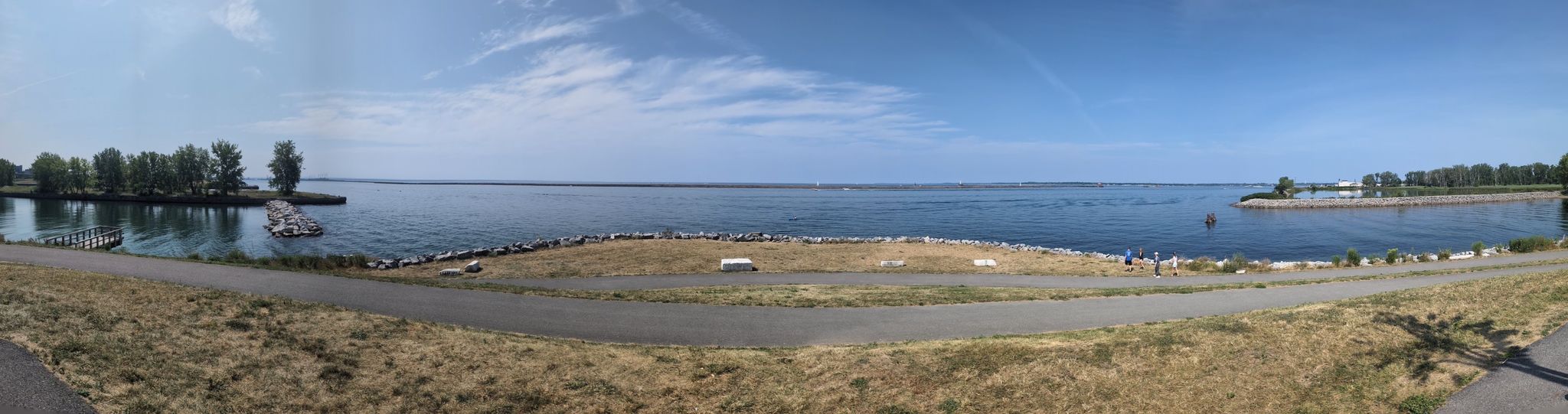Panoramic view of a wide bay under a clear sky, with a paved path. - Times Beach Nature Preserve loop