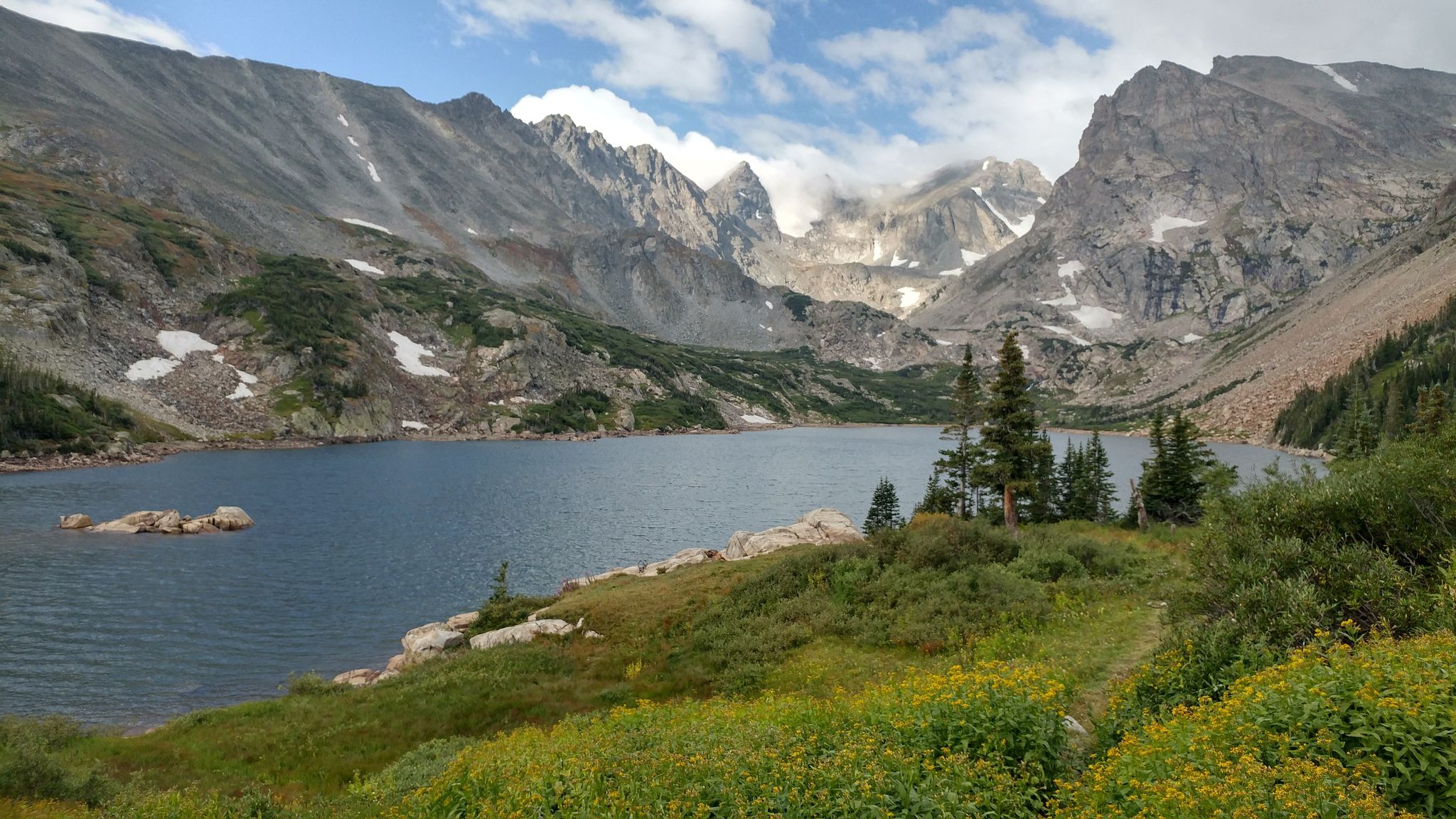 Large mountain lake with rocky shores, green hills, and distant peaks. - Lake Isabelle via Pawnee Pass Trail