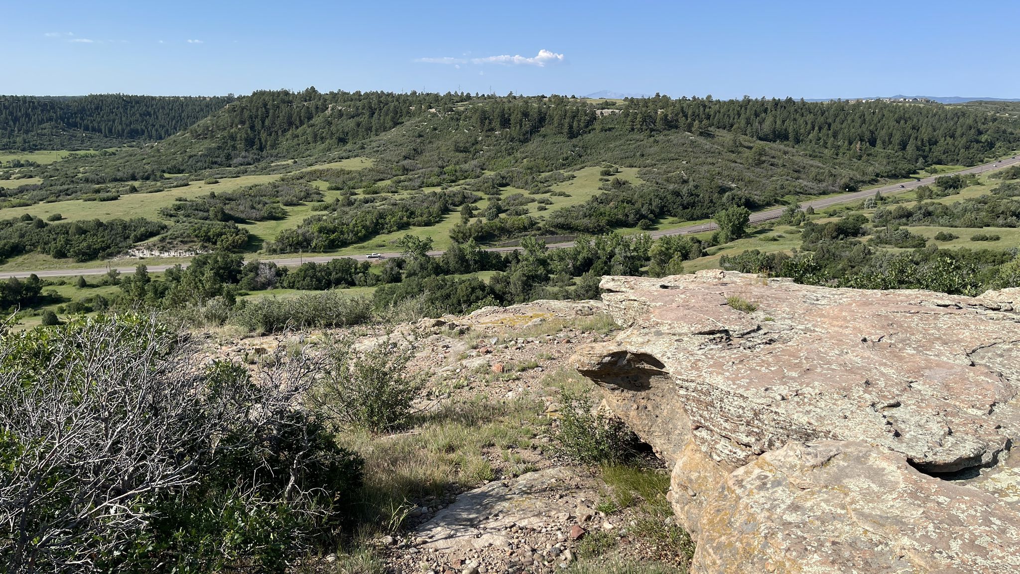 Sunny view from a rocky cliff overlooking a green valley and forested hills. - Mesa Rim Loop loop from Cobblestone Ranch Subdivision Park