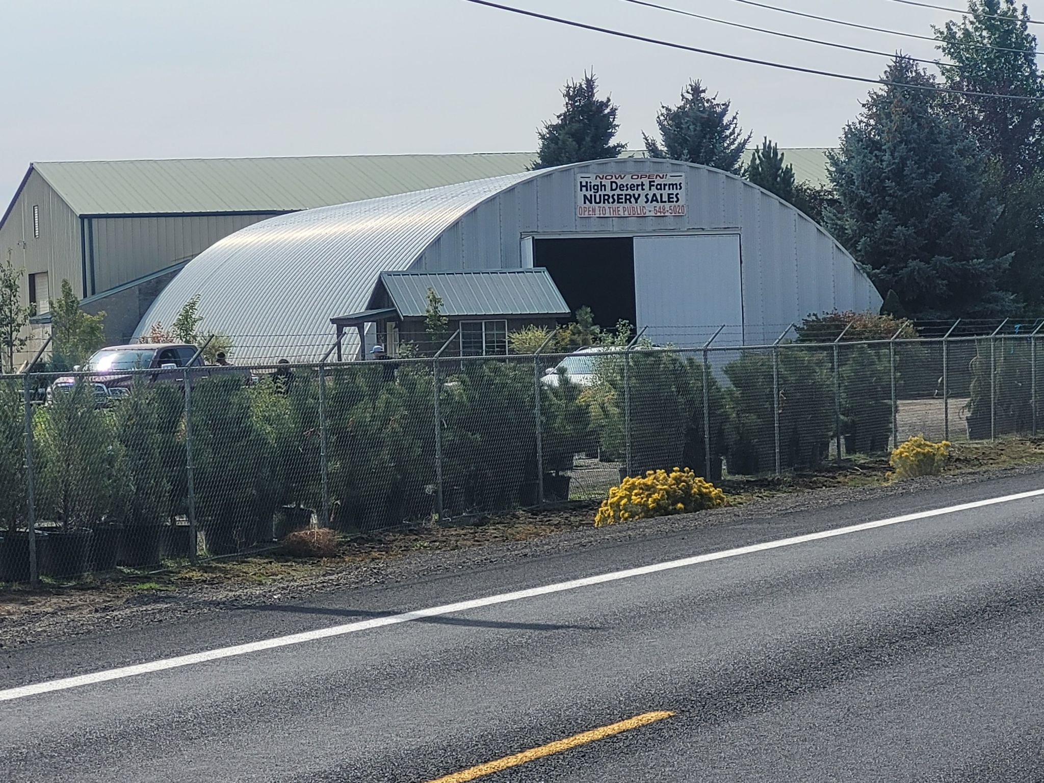 A large metal nursery building behind a chain-link fence on a sunny day. - Cline Falls Road & Old Bend Redmond Highway loop