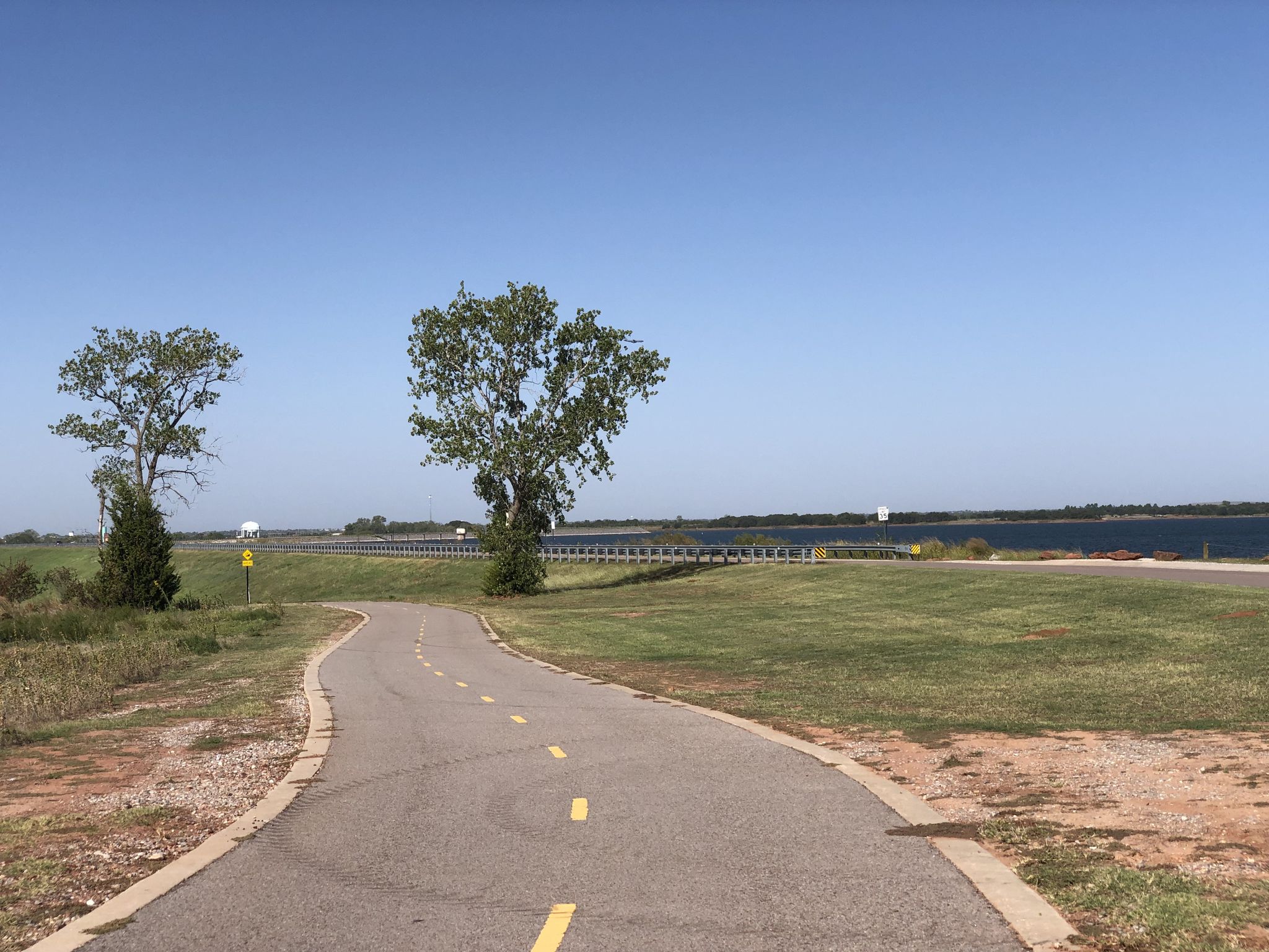 Paved path curves past two trees towards a large body of water. - Lake Stanley Draper loop from Lake Stanley Draper Park