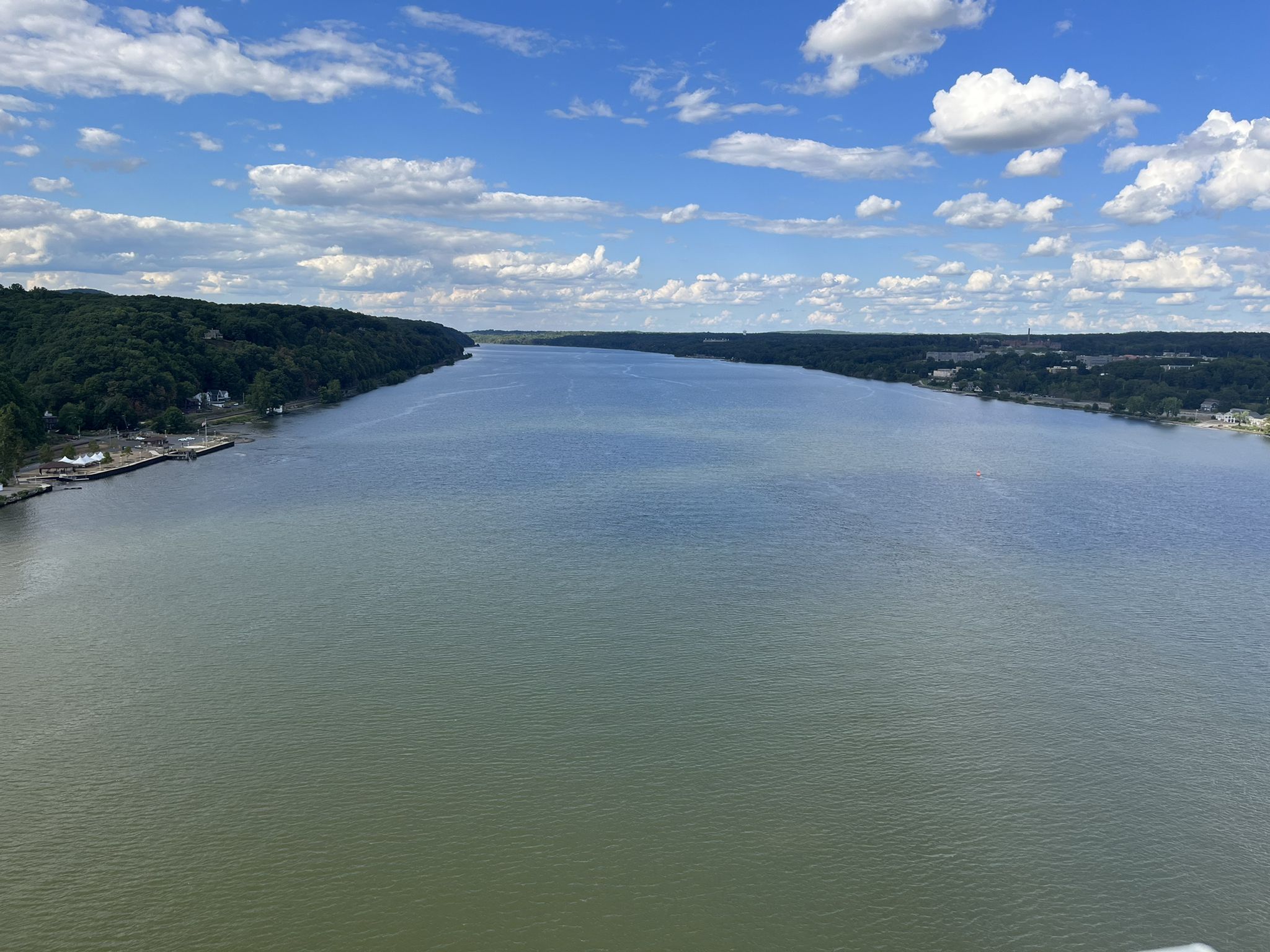 A wide river flows between green, forested banks under a blue sky. - Walkway Over the Hudson – Dutchess Rail Trail loop from Cold Spring