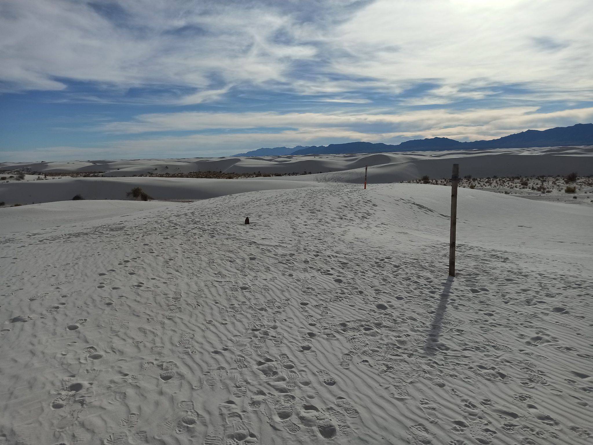 White sand dunes with footprints, distant mountains, and cloudy sky. - Backcountry Camping Loop Trail