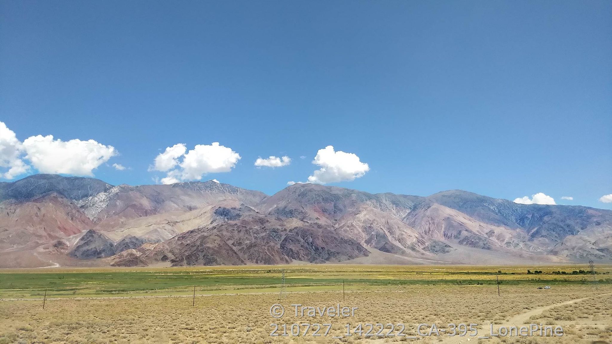 Vast arid plain with colorful mountains under a bright blue sky with clouds. - Manzanar loop