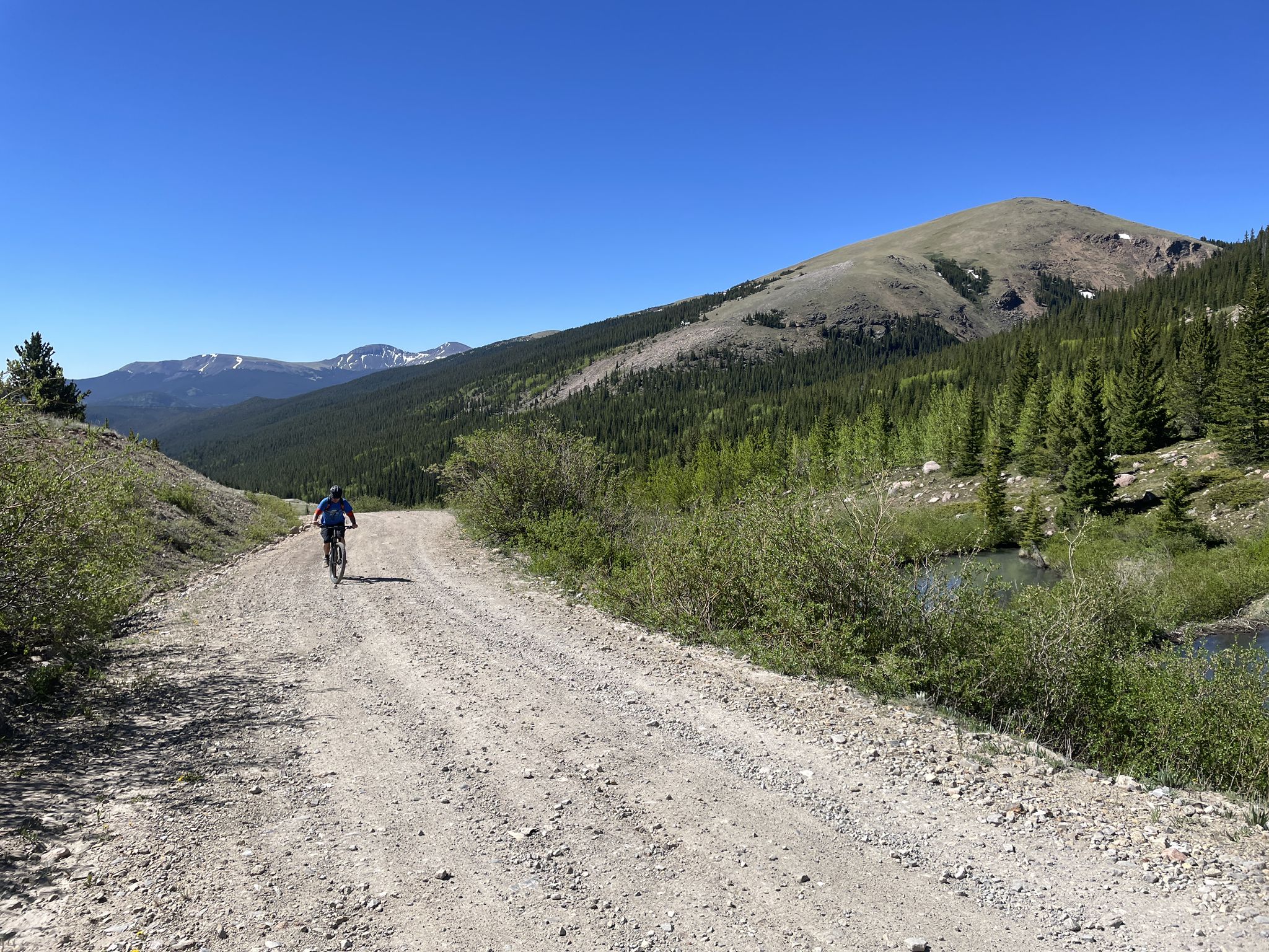 Person cycles on a sunny dirt mountain road beside a river. - Weston Pass Road