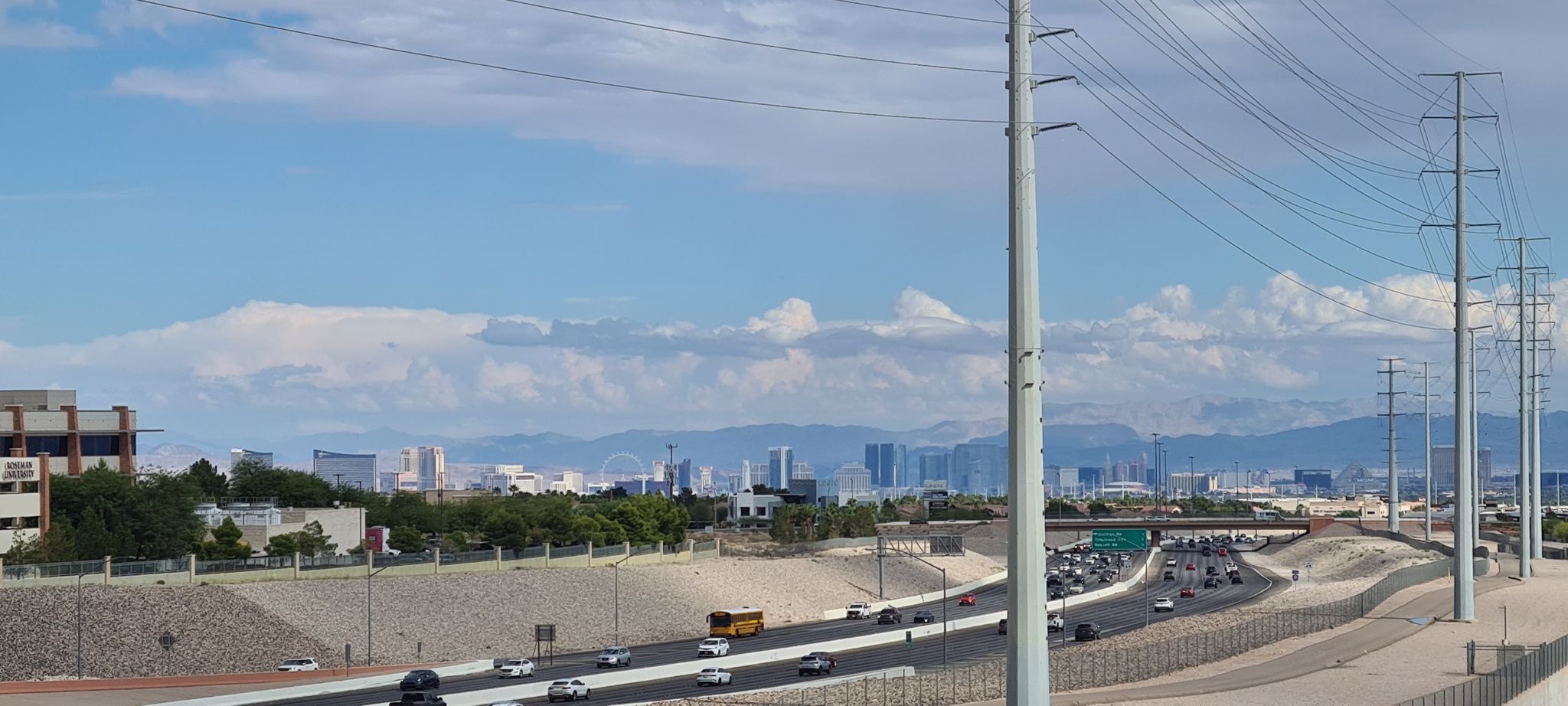 Busy highway with traffic, power lines, and a distant city skyline under clouds. - Northern Beltway Trail – Downtown Summerlin loop from Centennial Hills
