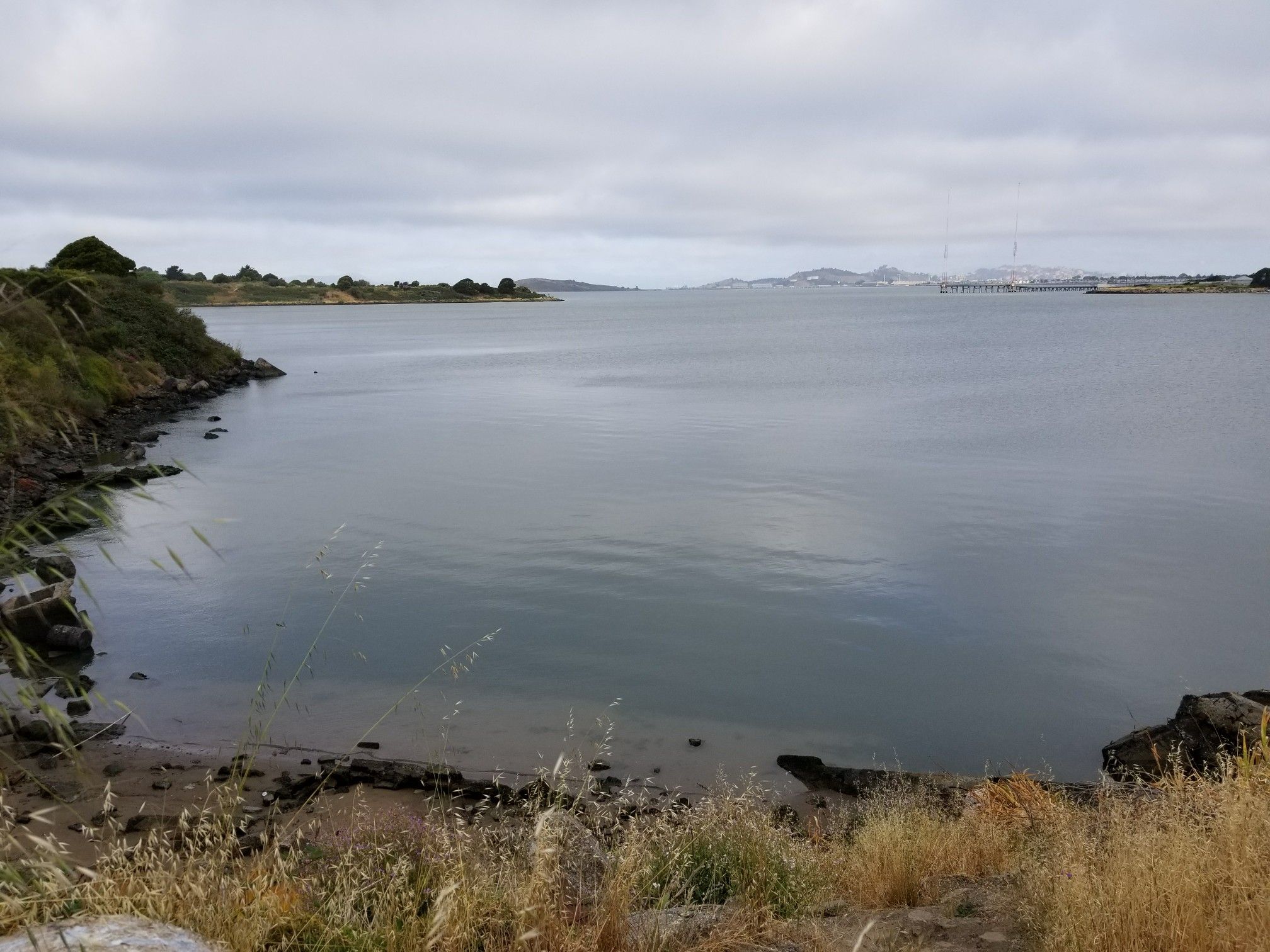Calm water by a rocky shore under an overcast sky. - Albany Waterfront Trail