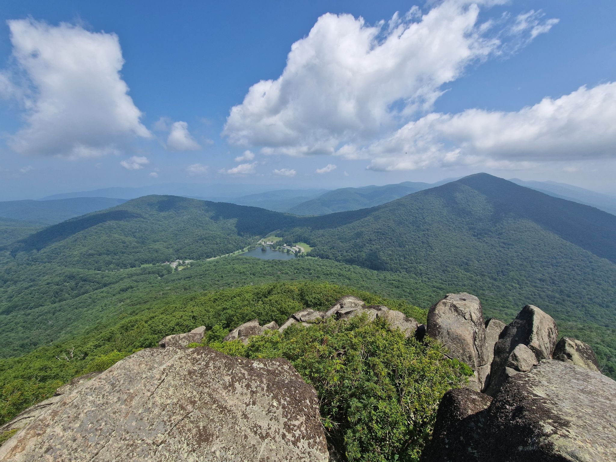 Expansive mountain vista from a rocky peak under a bright, cloudy sky. - Sharp Top Trail