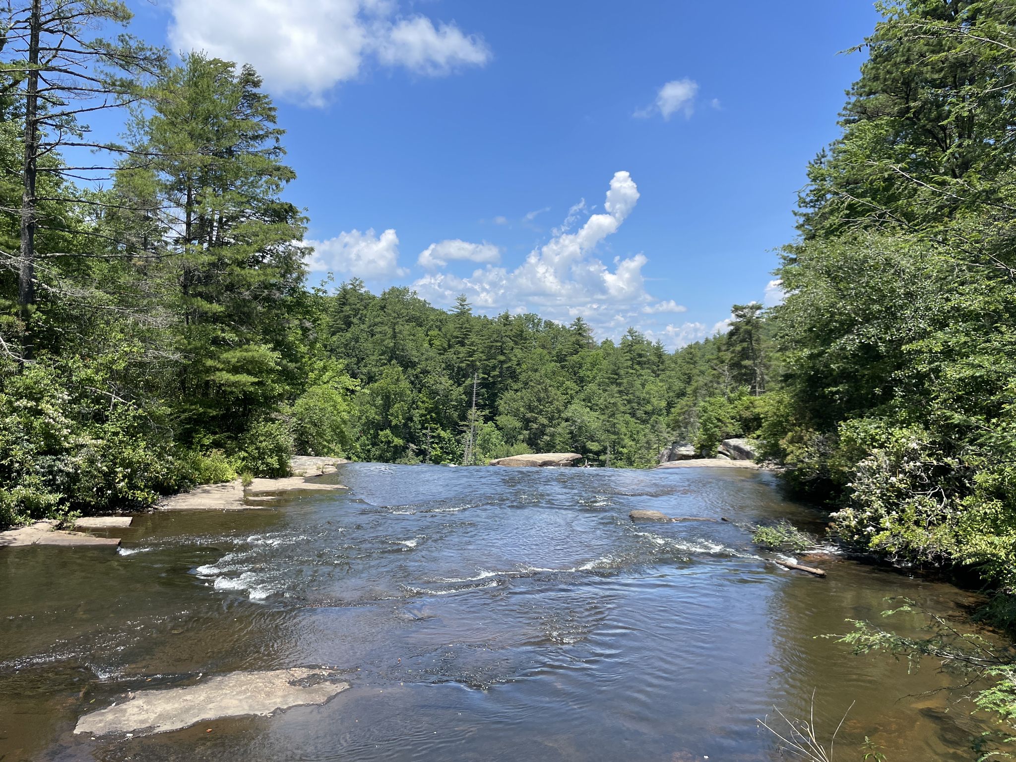 Wide river flowing over flat rocks, surrounded by green forest under a blue sky. - Hooker Falls, Triple Falls, Bridal Veil Falls, and High Falls Trail