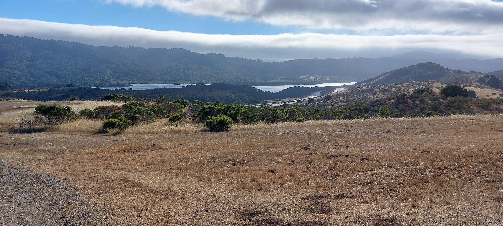 Dry hills overlooking a distant lake and mountains under a cloudy sky. - Hallmark Park Loop