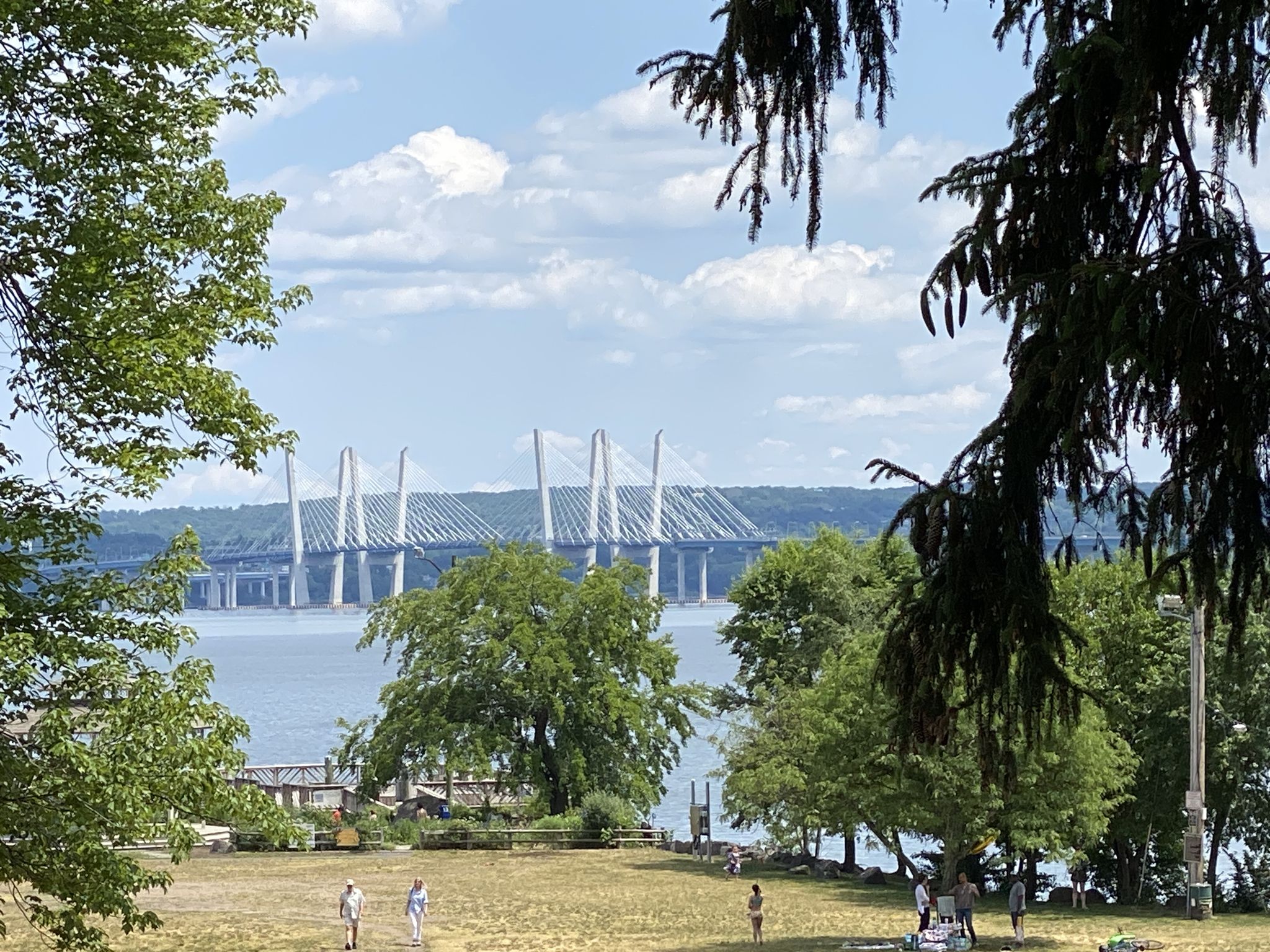 Large bridge over water, framed by trees, with people in a sunny grassy area. - Wild Duck Pond – Downtown Piermont loop from Glen Rock-Boro Hall