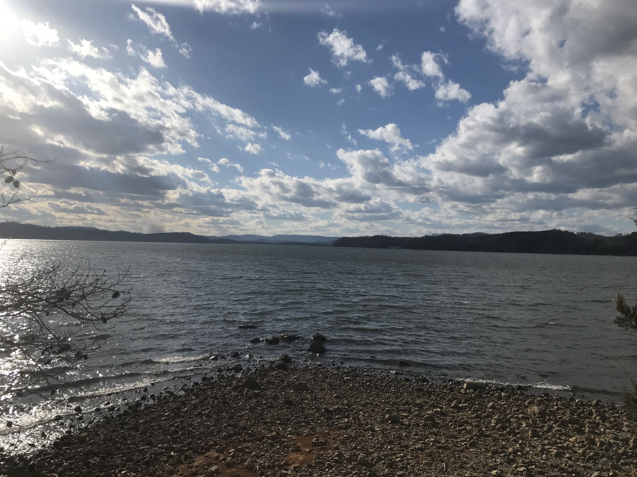 Sunlit lake with rocky shore under a partly cloudy sky. - Outer Loop Trail