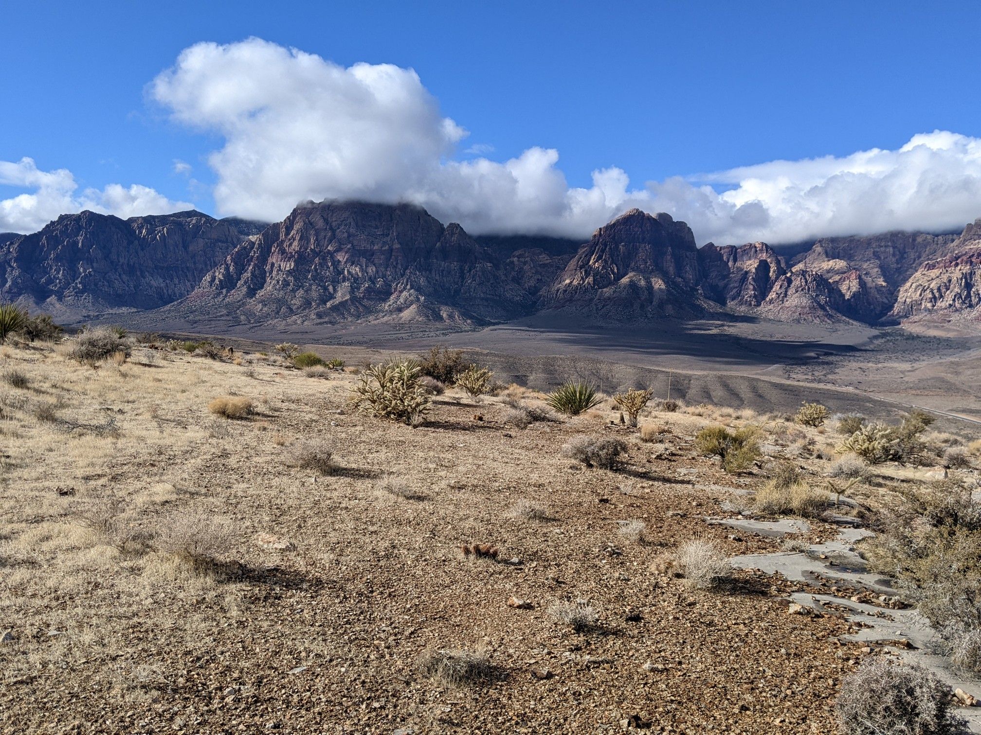 Wide desert vista with mountains partially obscured by white clouds. - Cowboy Trails Parking Lot – View of Red Rock Canyon loop from Red Rock Canyon Visitor Center