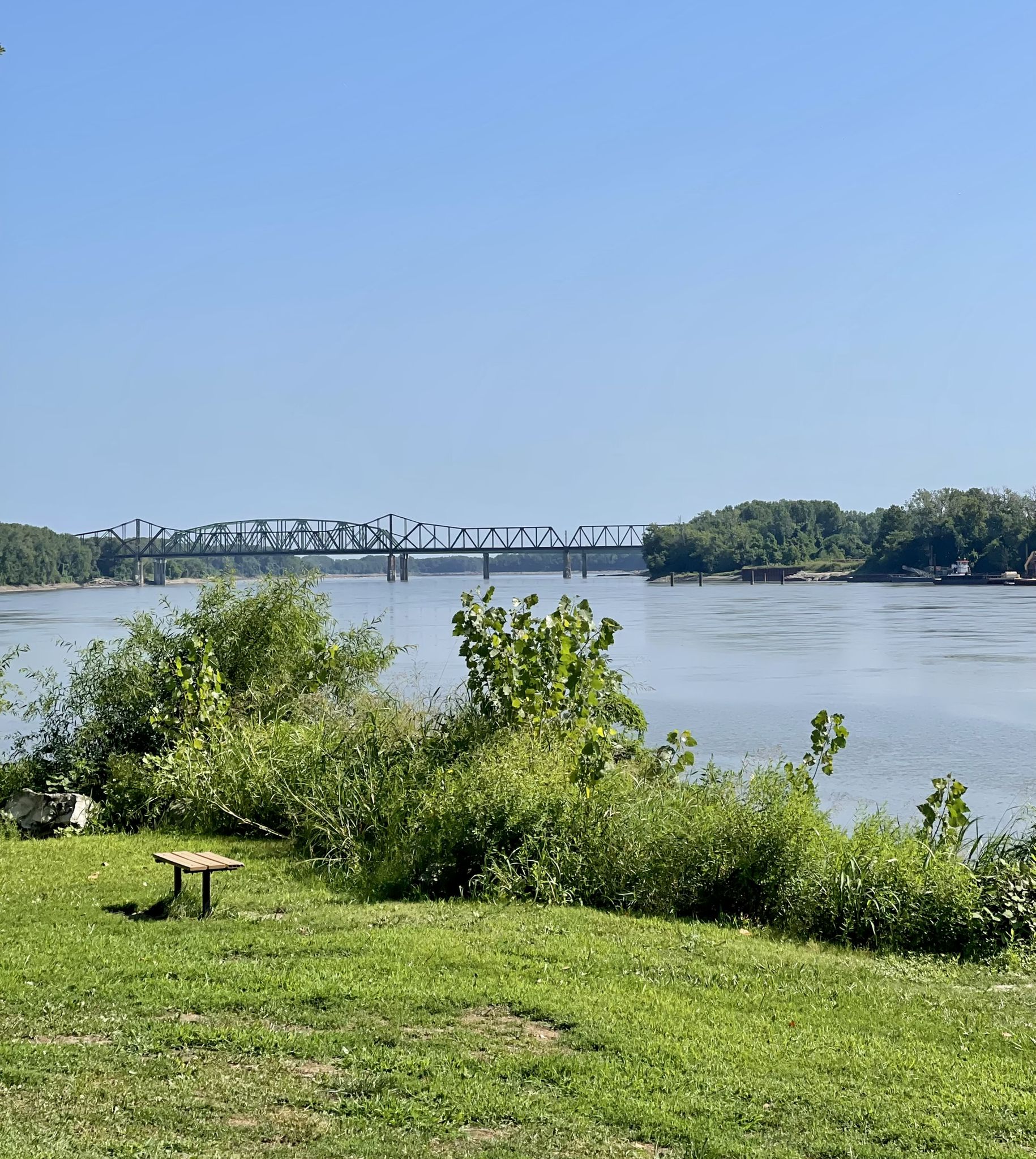 Wide river view with a distant truss bridge and green, sunny banks. - Katy Trail and Historic St. Charles Loop