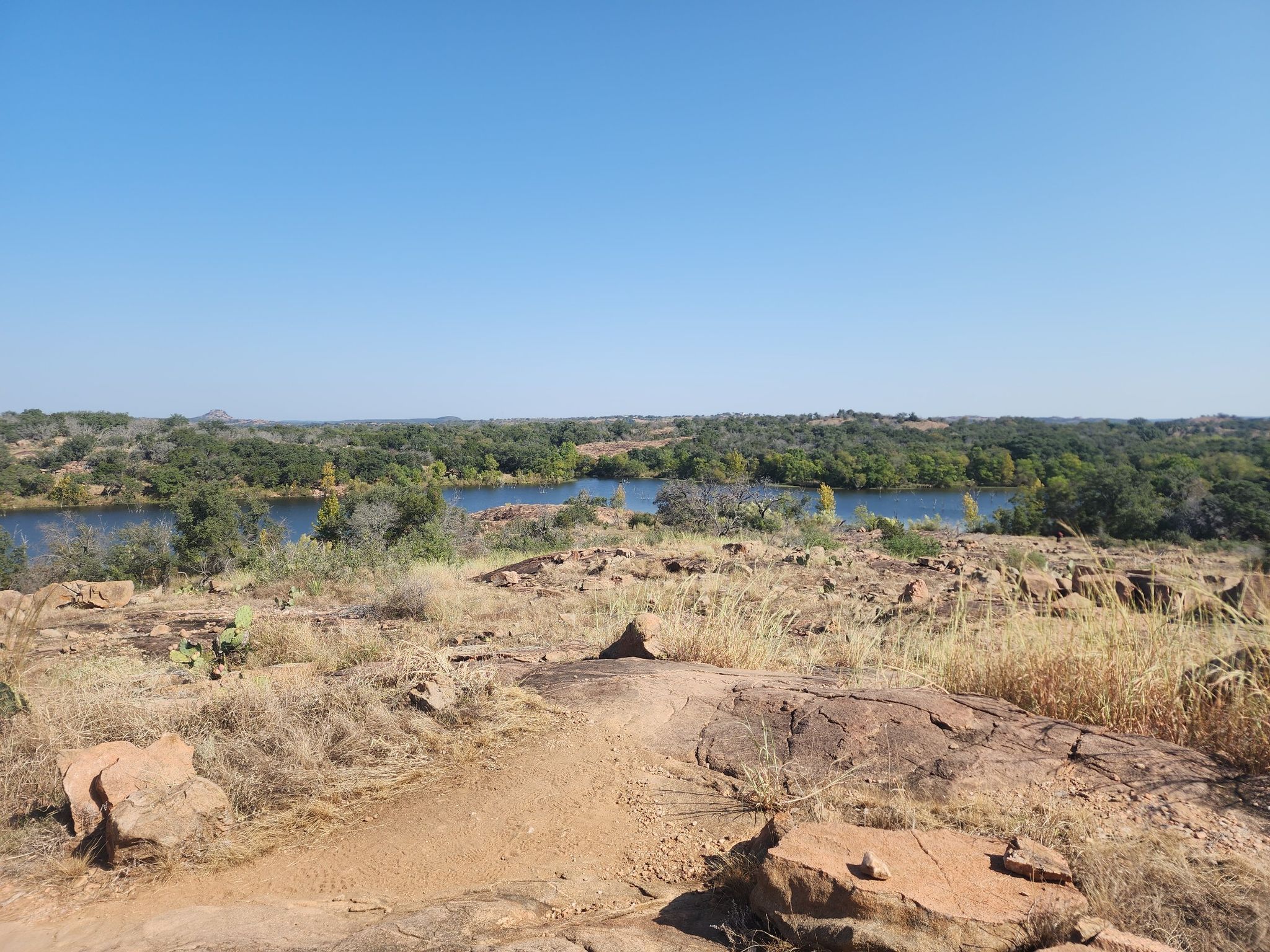 Rocky foreground overlooking a calm lake surrounded by green forest under a clear sky. - 1000ft overlook of Inks Lake loop from Inks Lake State Park