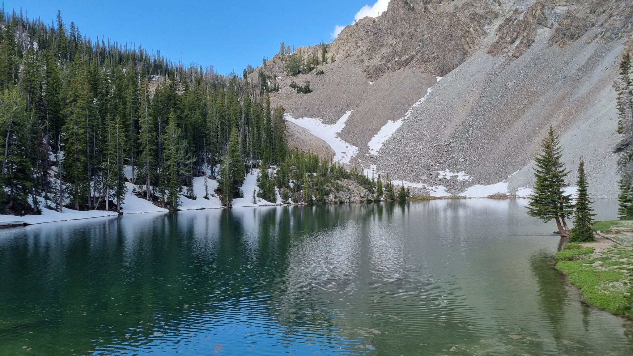 Serene mountain lake with pine trees and snow-dusted rocky slopes on a clear day. - Norton Lake Trail