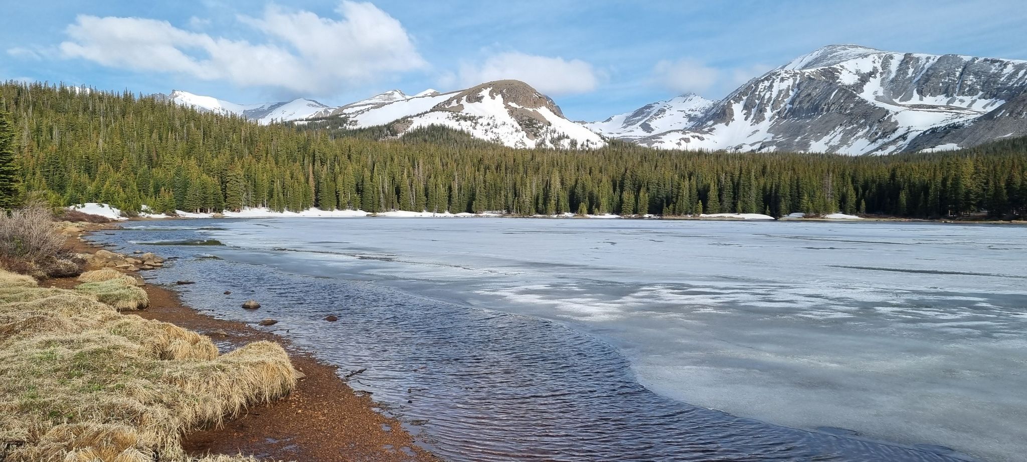 Partially frozen lake with pine forest and snow-capped mountains under a bright sky. - CMC South Trail and Little Raven Trail