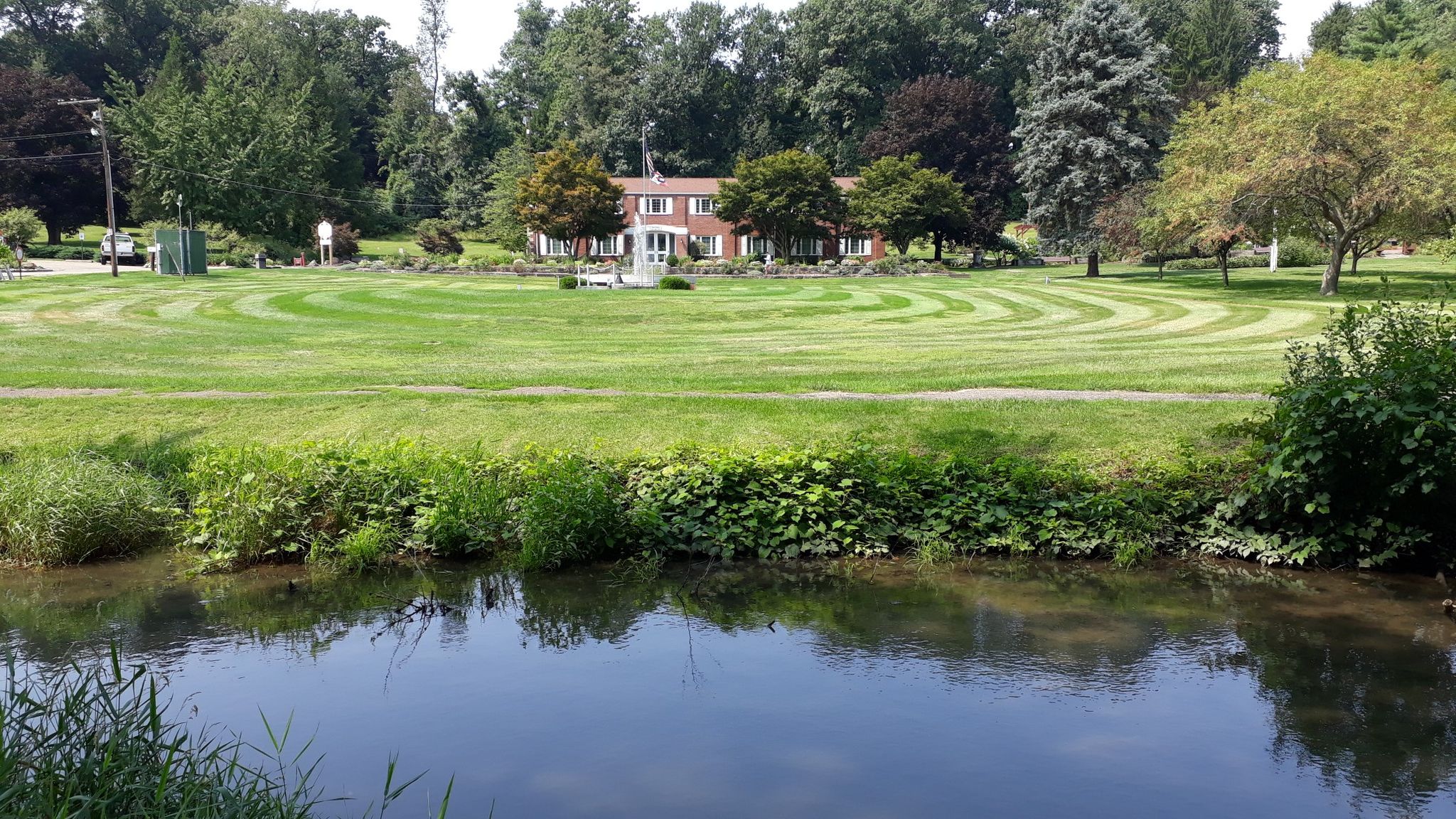 Sunny view of a large house and patterned lawn reflected in calm water. - Herbert L. Fisher Walking Track