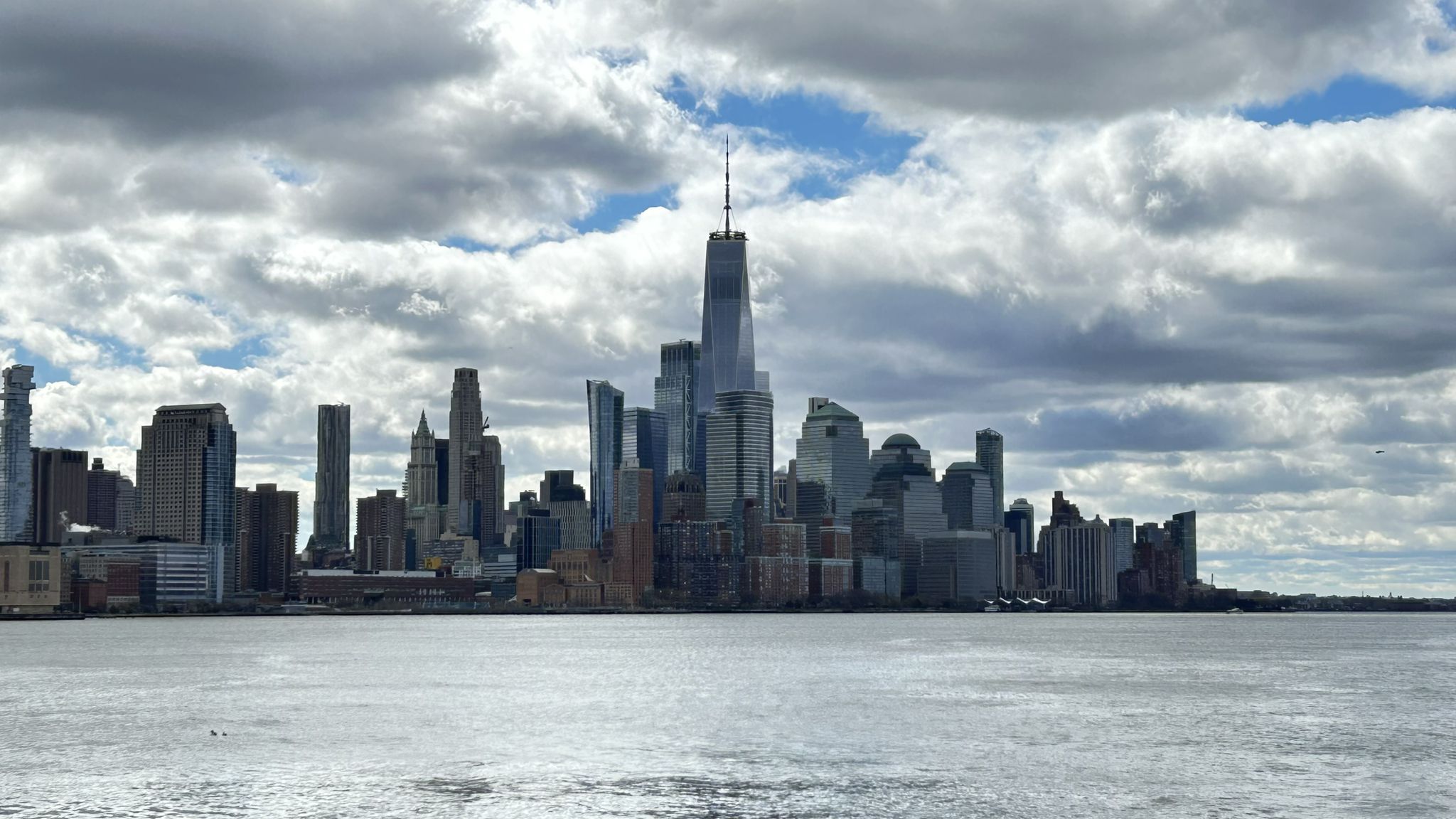 City skyline across water under a dramatic cloudy sky. - Hoboken Terminal – Weehawken Cove loop from 2nd Street