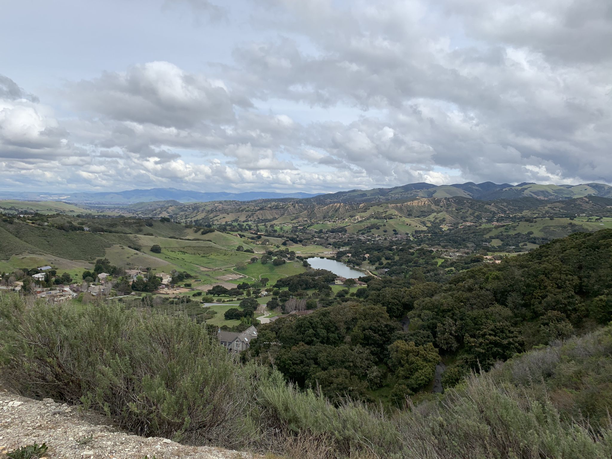 A wide valley with rolling green hills, a lake, under cloudy skies. - Roadbike loop from WeatherTech Raceway Laguna Seca