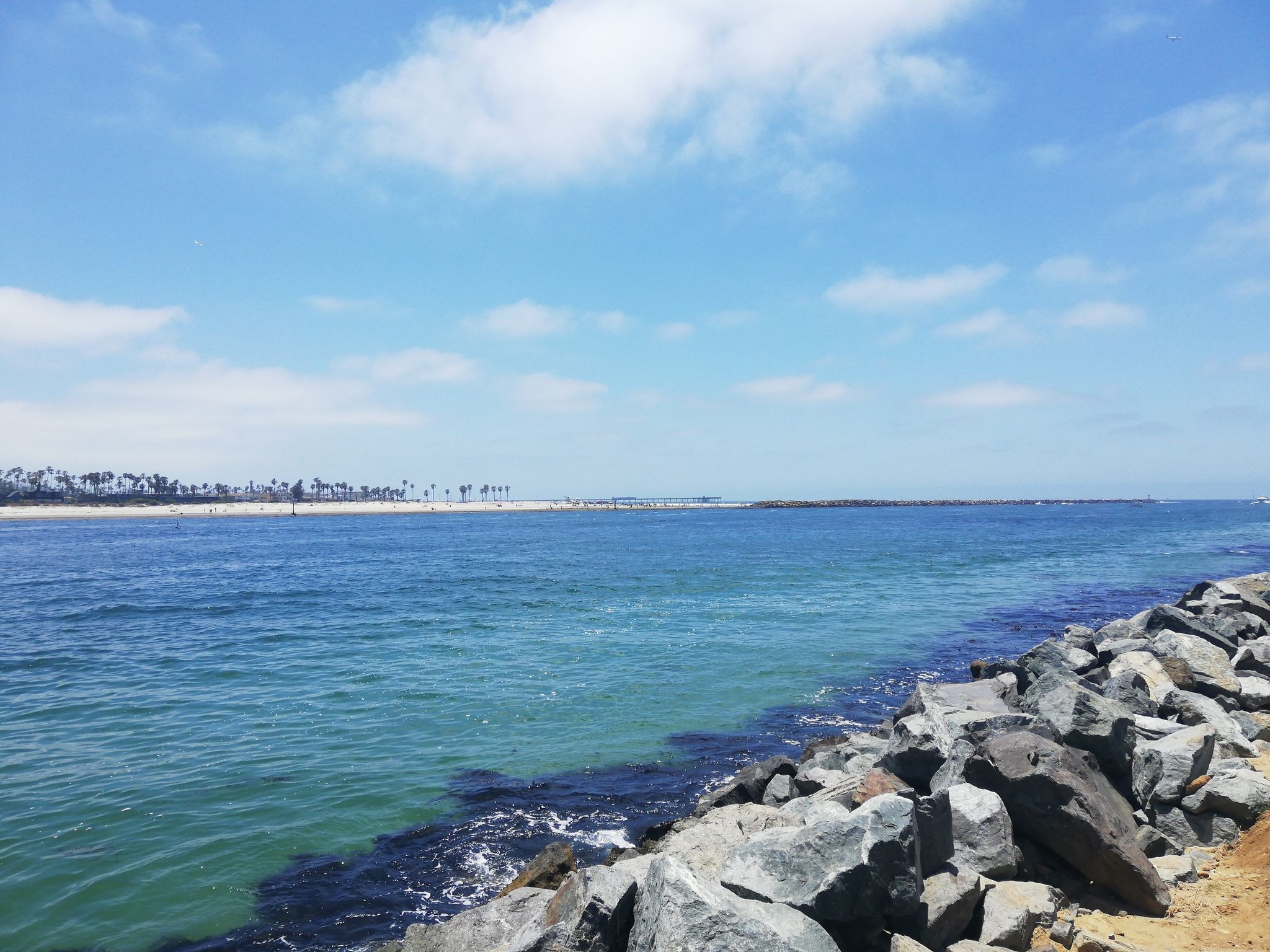 Bright blue ocean meets a rocky shore under a sunny sky. - Ocean Front Walk – Mission Bay loop from Pacific Beach